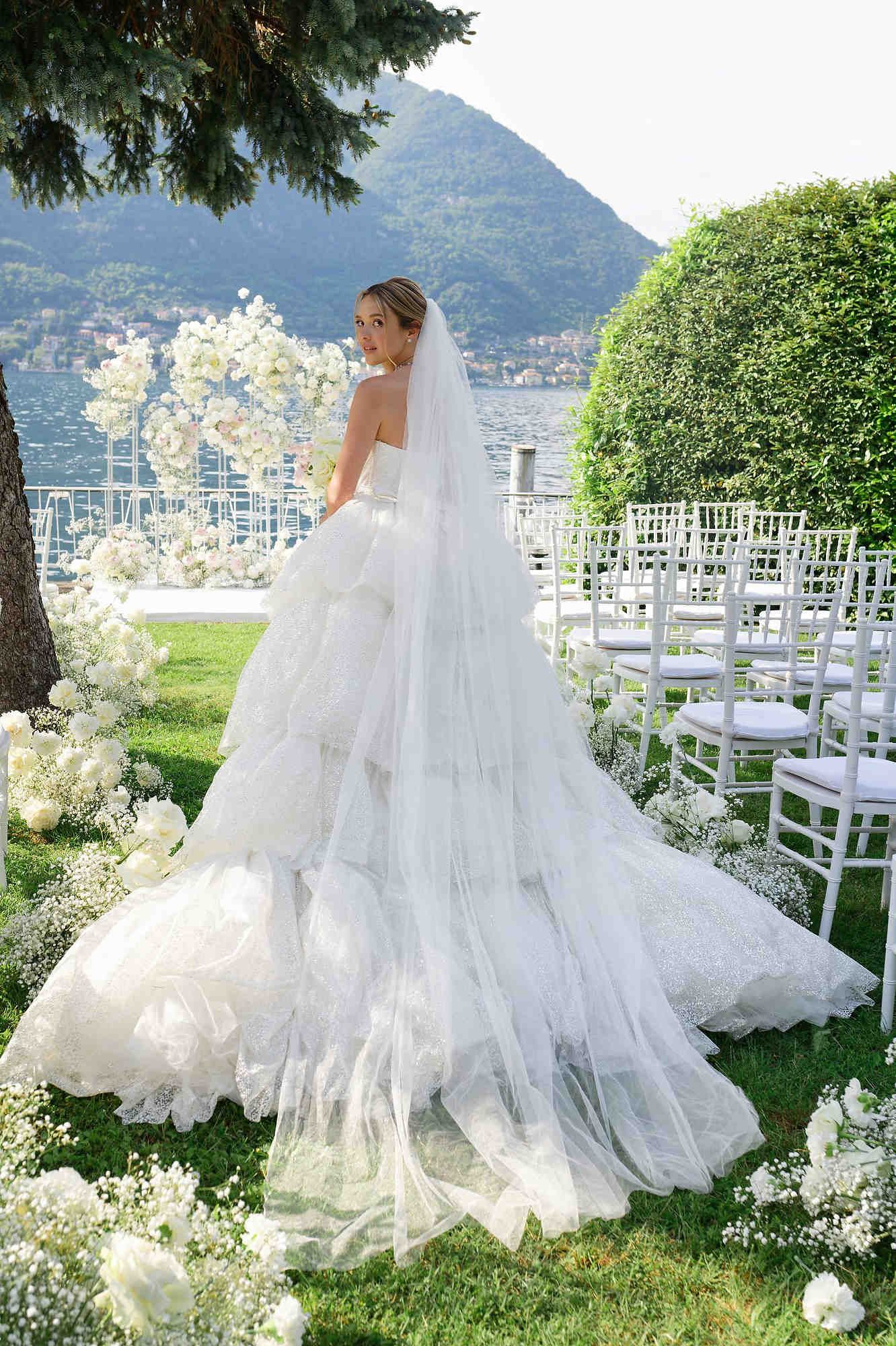 A stunning bride in a luxury wedding gown with a long train posing against the breathtaking mountain and lake backdrop of Lake Como, Italy.