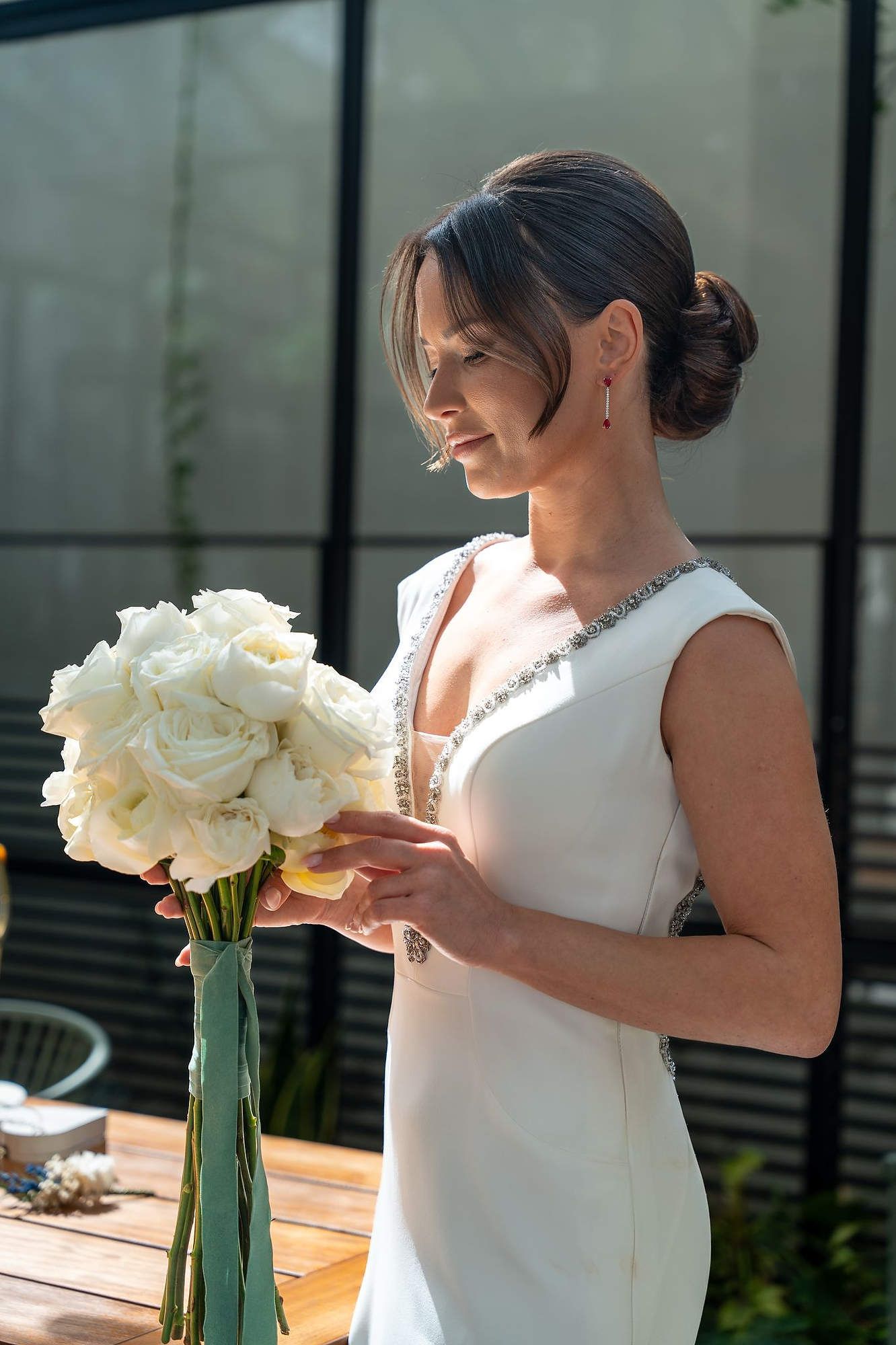 Elegant bride with classic bridal makeup and hair styling looking at her bouquet at El Telar de Miguel Martí, Valencia.