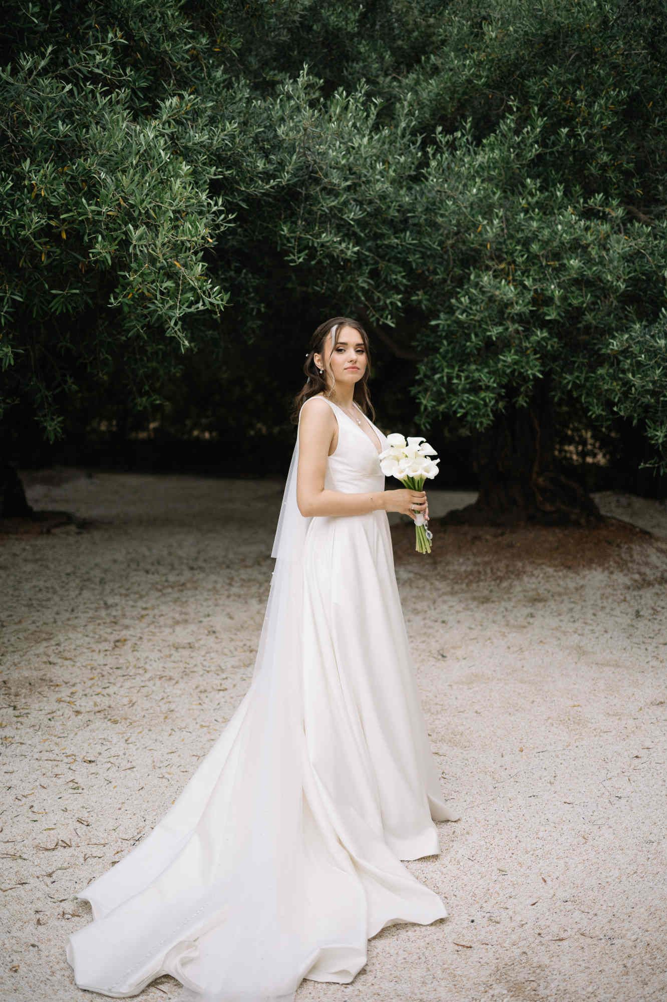 Bride with a long dress train and calla lily bouquet in the olive garden of Alqueria del Xúquer, Valencia wedding venue.