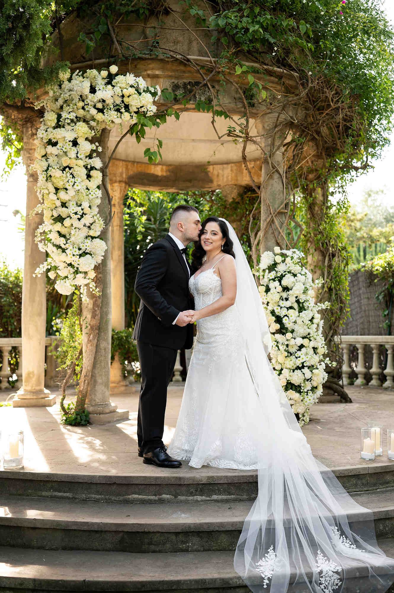 The bride and groom standing on the decorated ceremony podium at Casa Santonja surrounded by floral arrangements