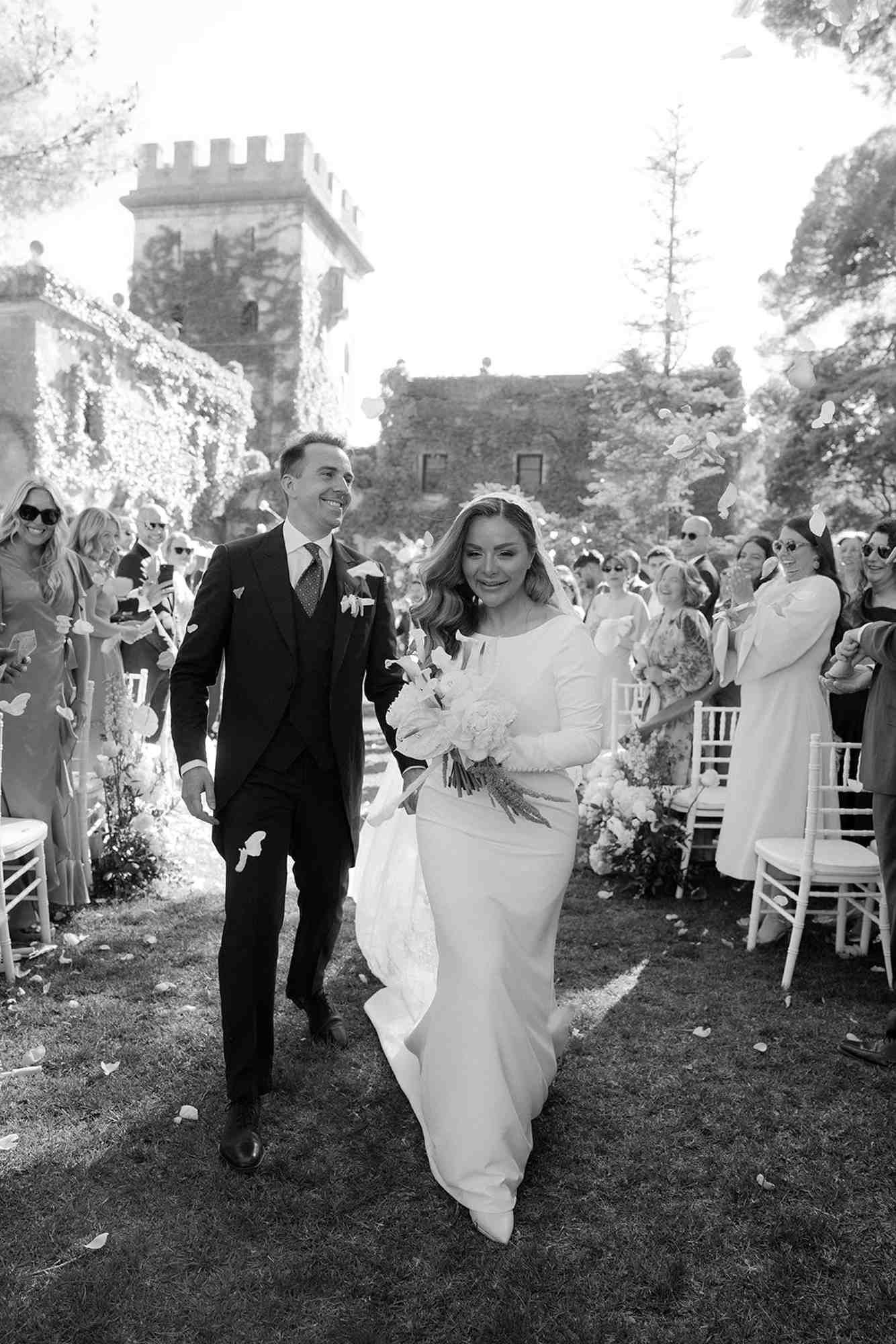 Newlyweds walking through a crowd of guests throwing white rose petals. Joyful wedding exit at Finca Torrefiel venue in Valencia.