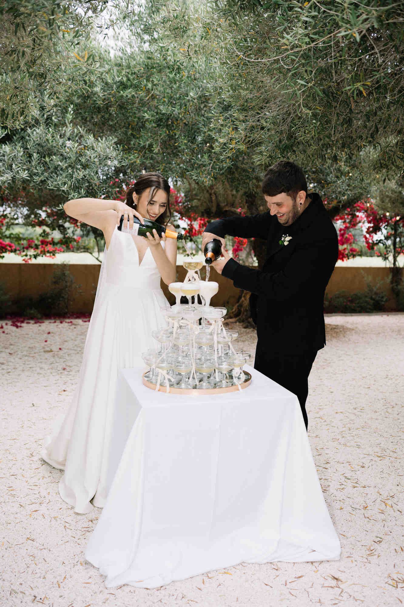 Bride and groom pouring champagne into a glass tower during their wedding celebration at the Alqueria del Xúquer estate in Valencia.