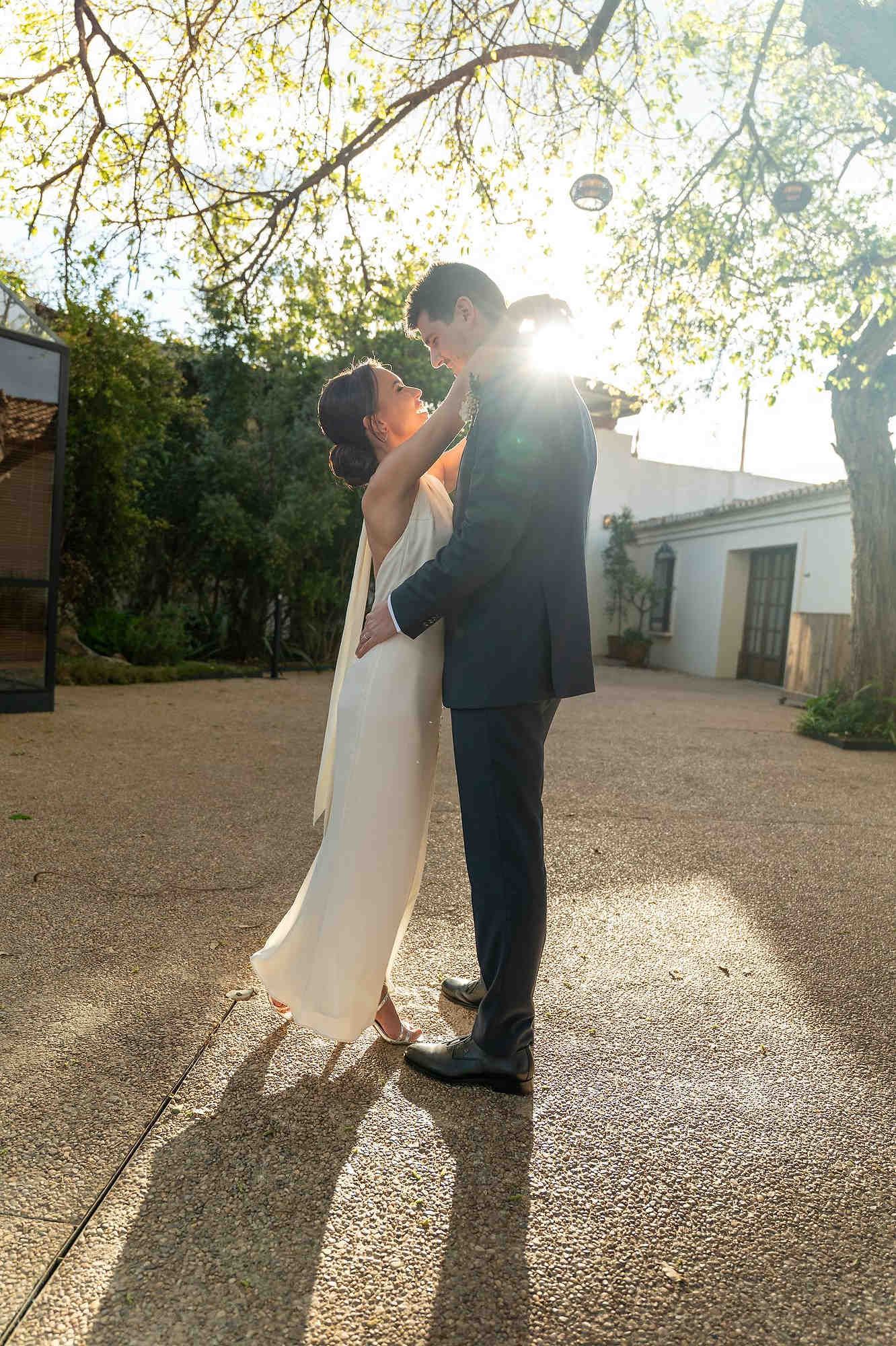 Romantic moment of the groom embracing the bride in the courtyard of El Telar de Miguel Martí, showcasing professional bridal styling