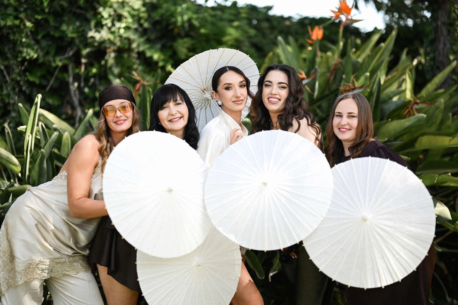 Bride and bridesmaids with elegant makeup and hairstyles posing with sun parasols during a wedding photoshoot at Villa Paula.