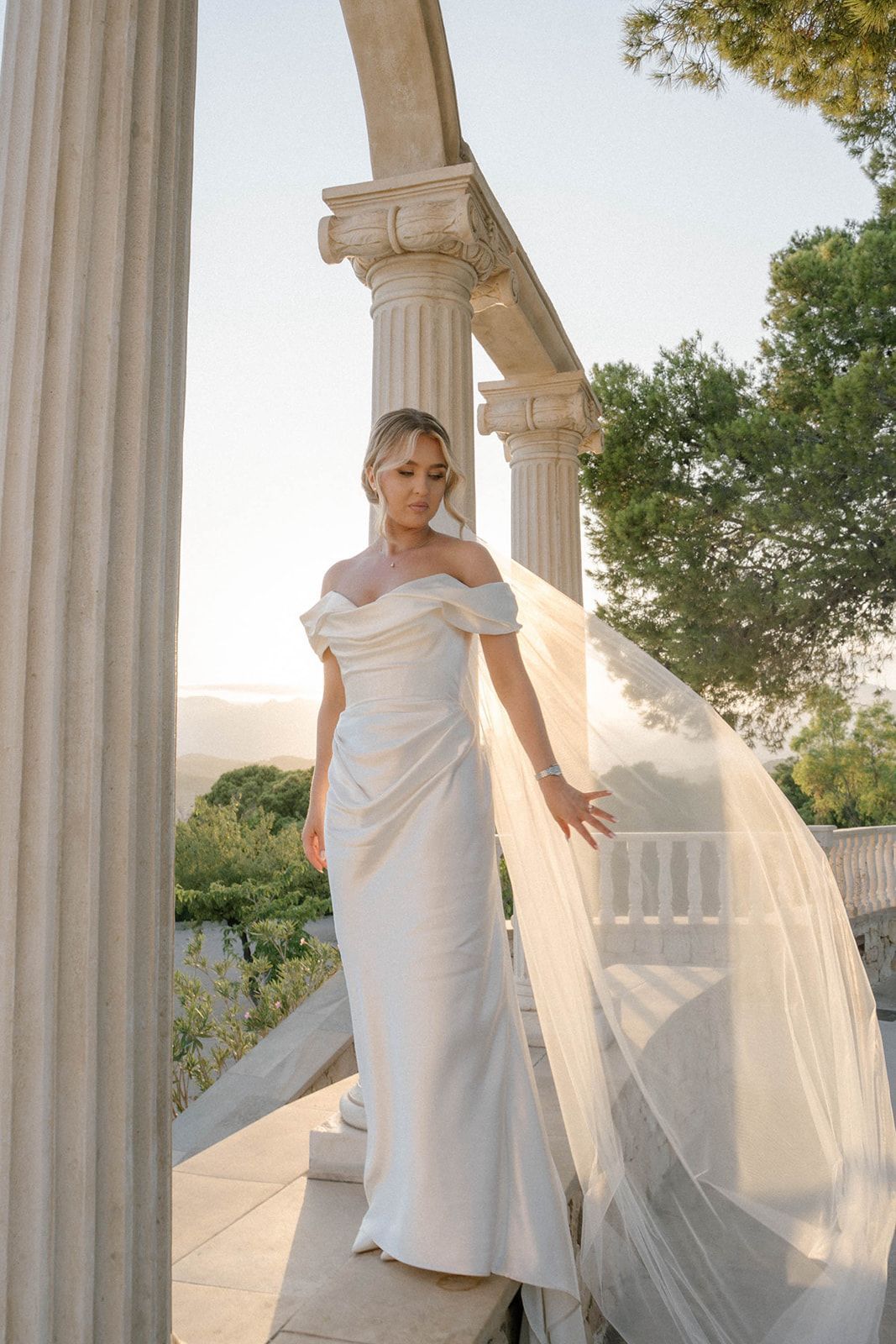 Bride with a long wedding veil posing in the golden sunset light at Finca Marqués de Montemolar with makeup and hair by Anastasia Larionova.