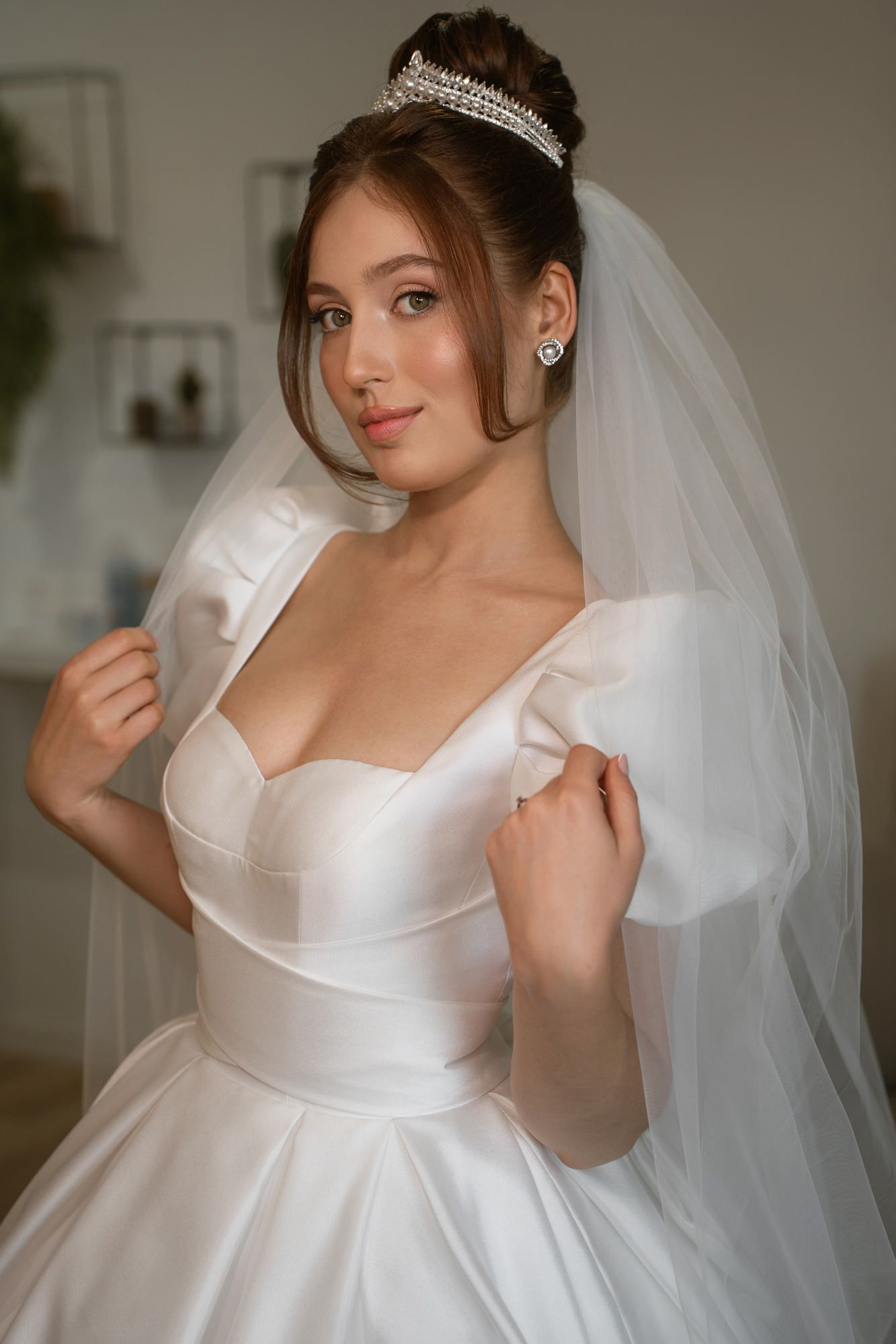 Bride with a polished bun and tiara adjusting her veil. Professional wedding hair styling and makeup for a luxury celebration in Spain.