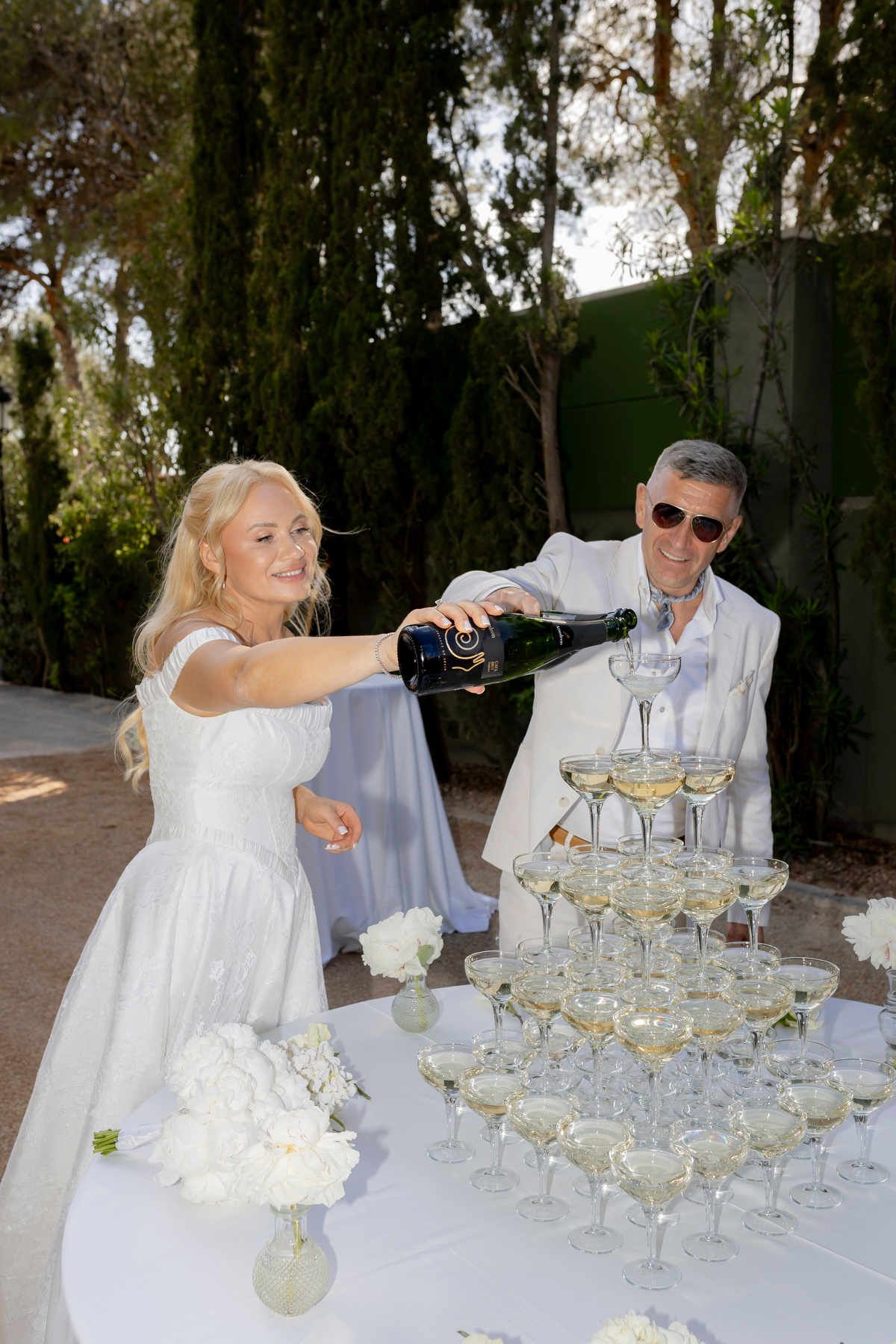Bride pouring champagne at Finca Marqués de Montemolar; her radiant makeup holds perfectly in the bright Mediterranean light.