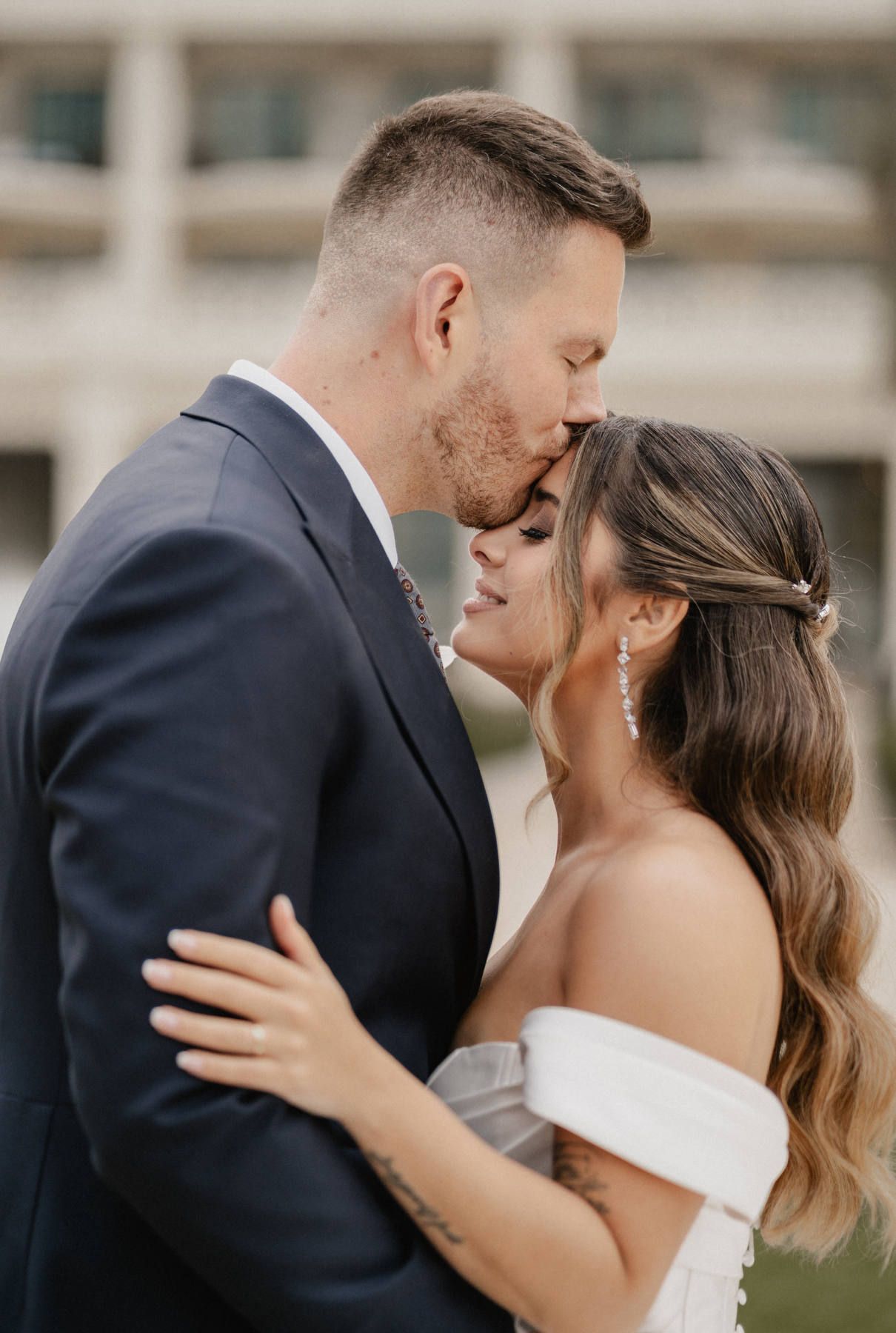 Groom kissing the bride; close-up showing her nude satin lip, softly defined eyes, and polished waves holding up beautifully.