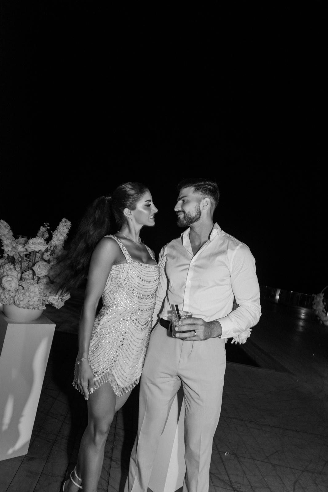 Bride in a second dress and groom with cocktail glasses during a stylish post-wedding party, showing a refreshed evening bridal beauty look.