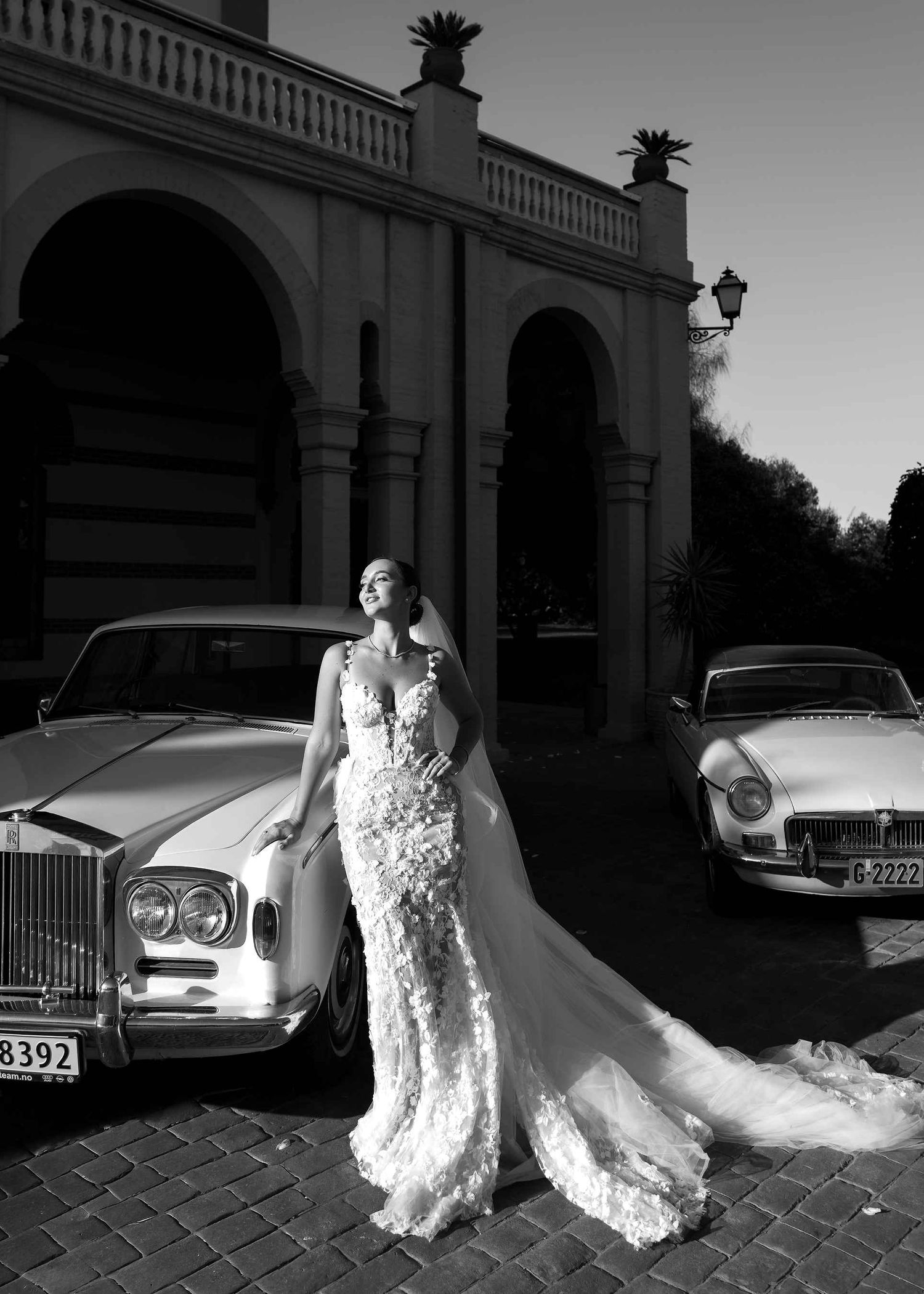 Full-length bridal portrait with a luxury car and hard light, featuring professional styling against the Gran Villa Rosa backdrop