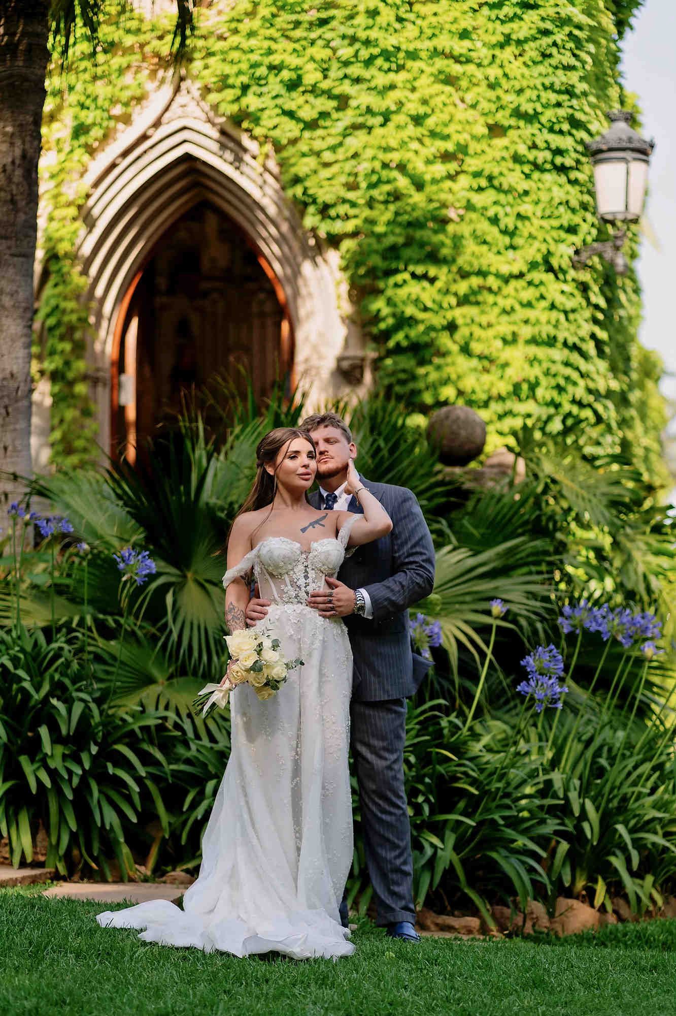 Romantic moment with the groom hugging the bride from behind in front of the ornate wooden doors in the courtyard of Casa Santonja.