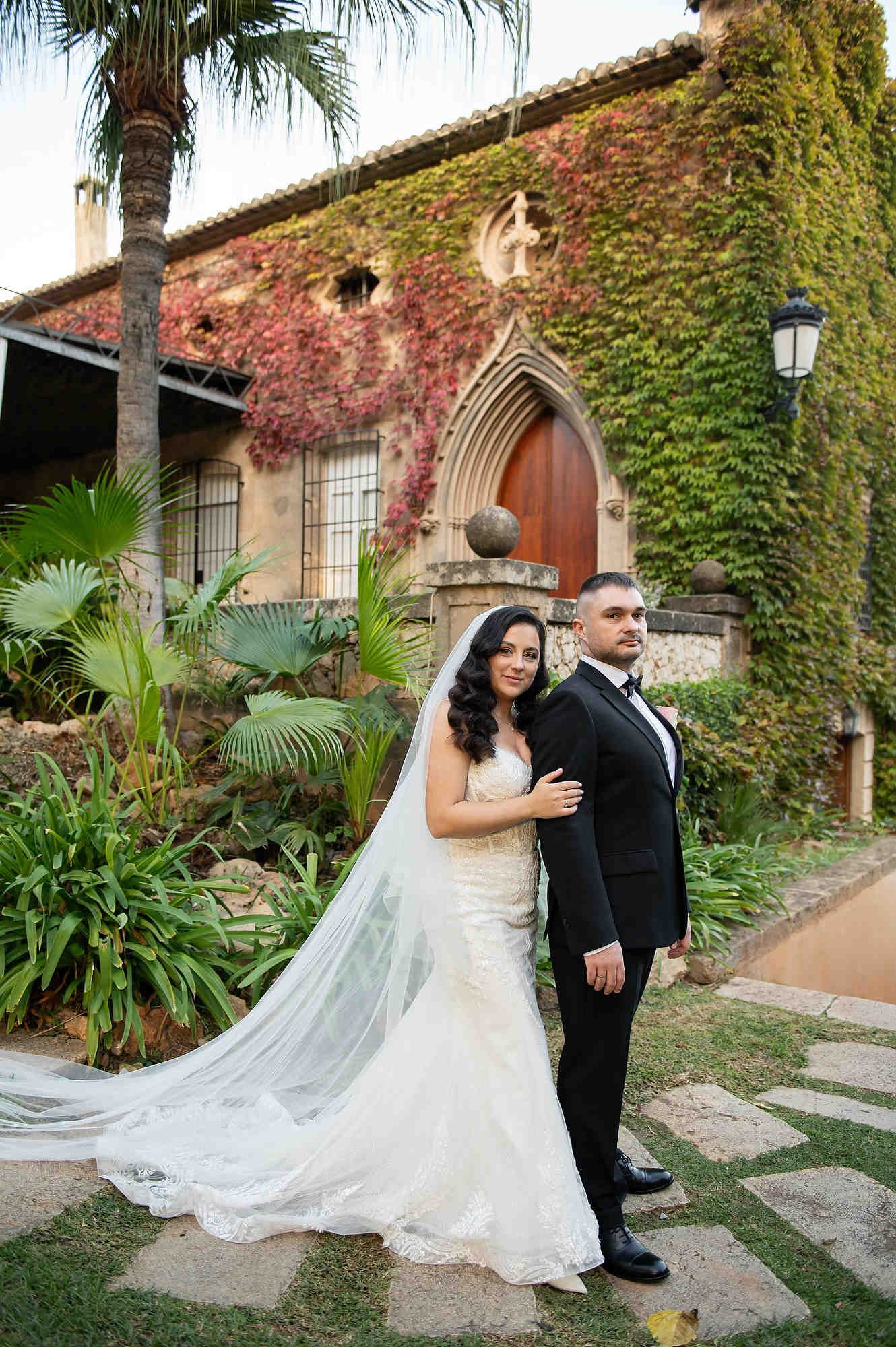 The wedding couple posing against the historic gates of Casa Santonja covered in vibrant red autumn ivy leaves.