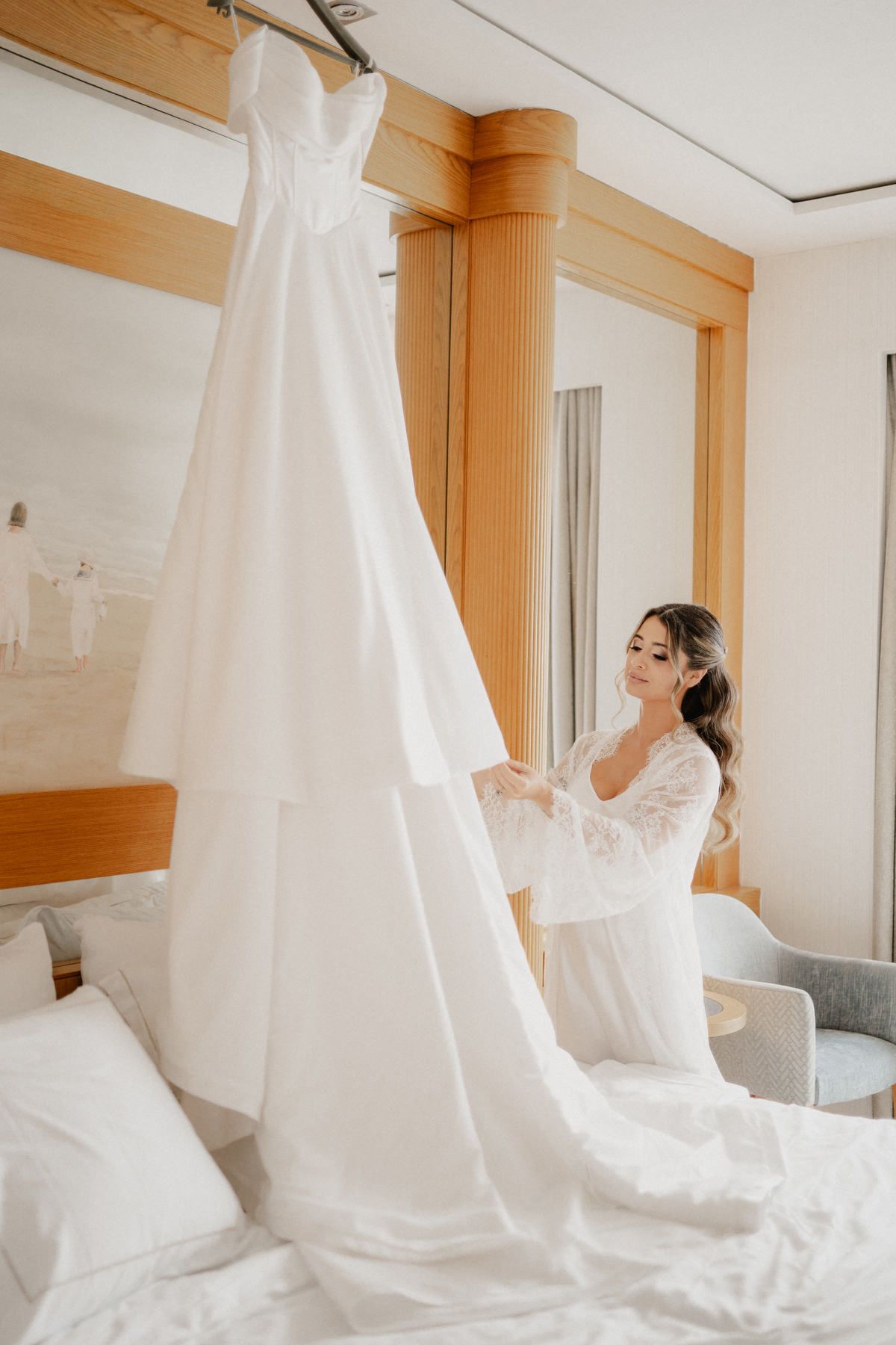 Bride admiring her dress in a light-filled suite at Las Arenas, showcasing her loose, polished waves in a beautiful half-up style.