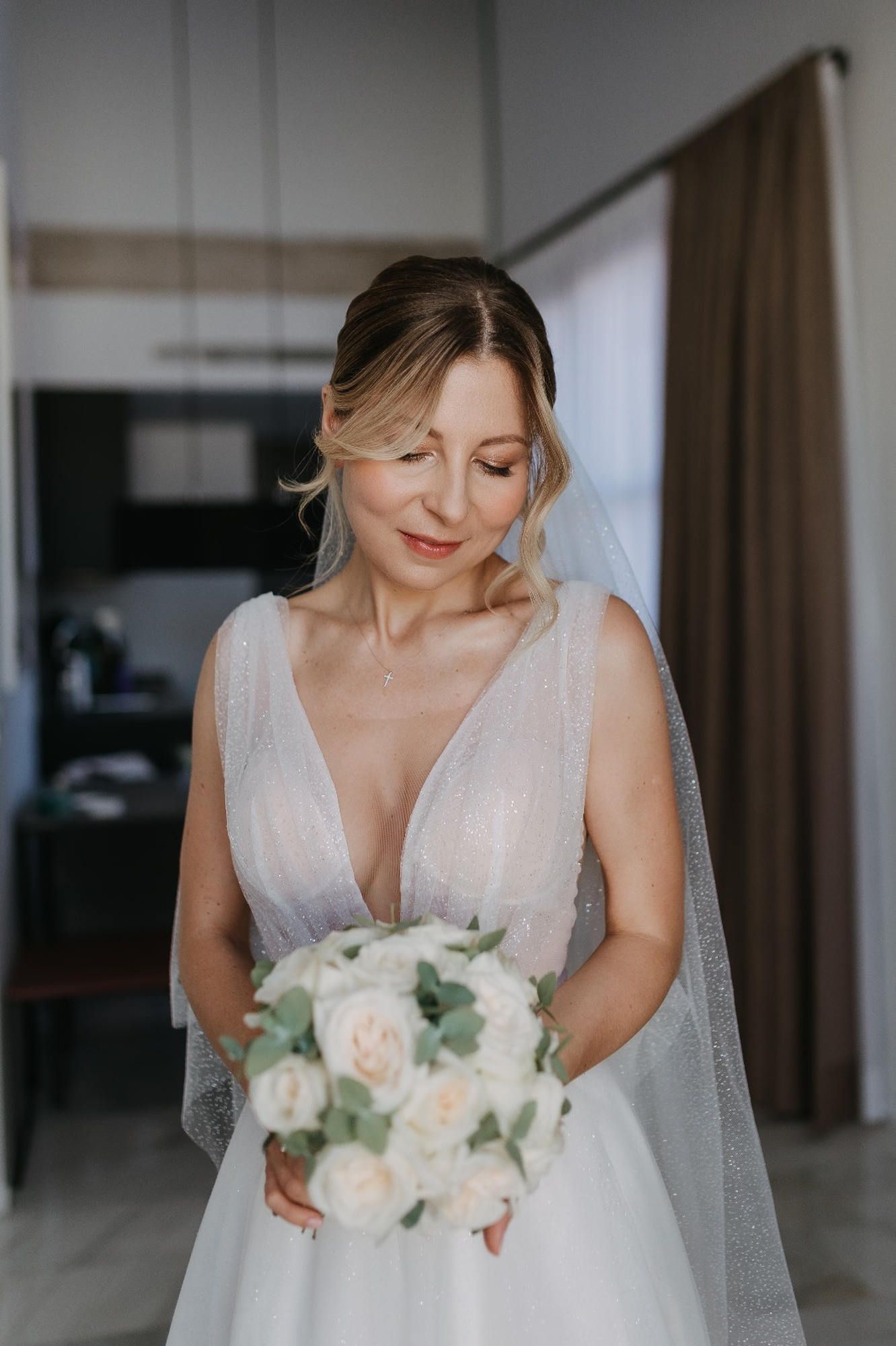 A bride in Valencia admiring her wedding bouquet, showcasing a sophisticated editorial bridal makeup design and elegant hair styling
