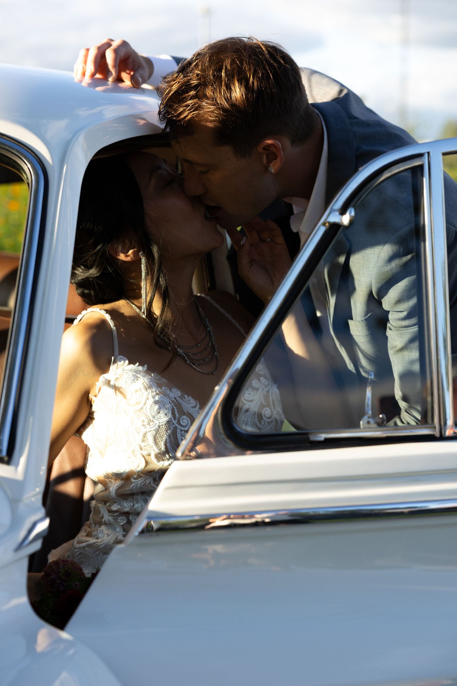 A romantic moment captured between newlyweds sharing a kiss inside a classic white vintage car.