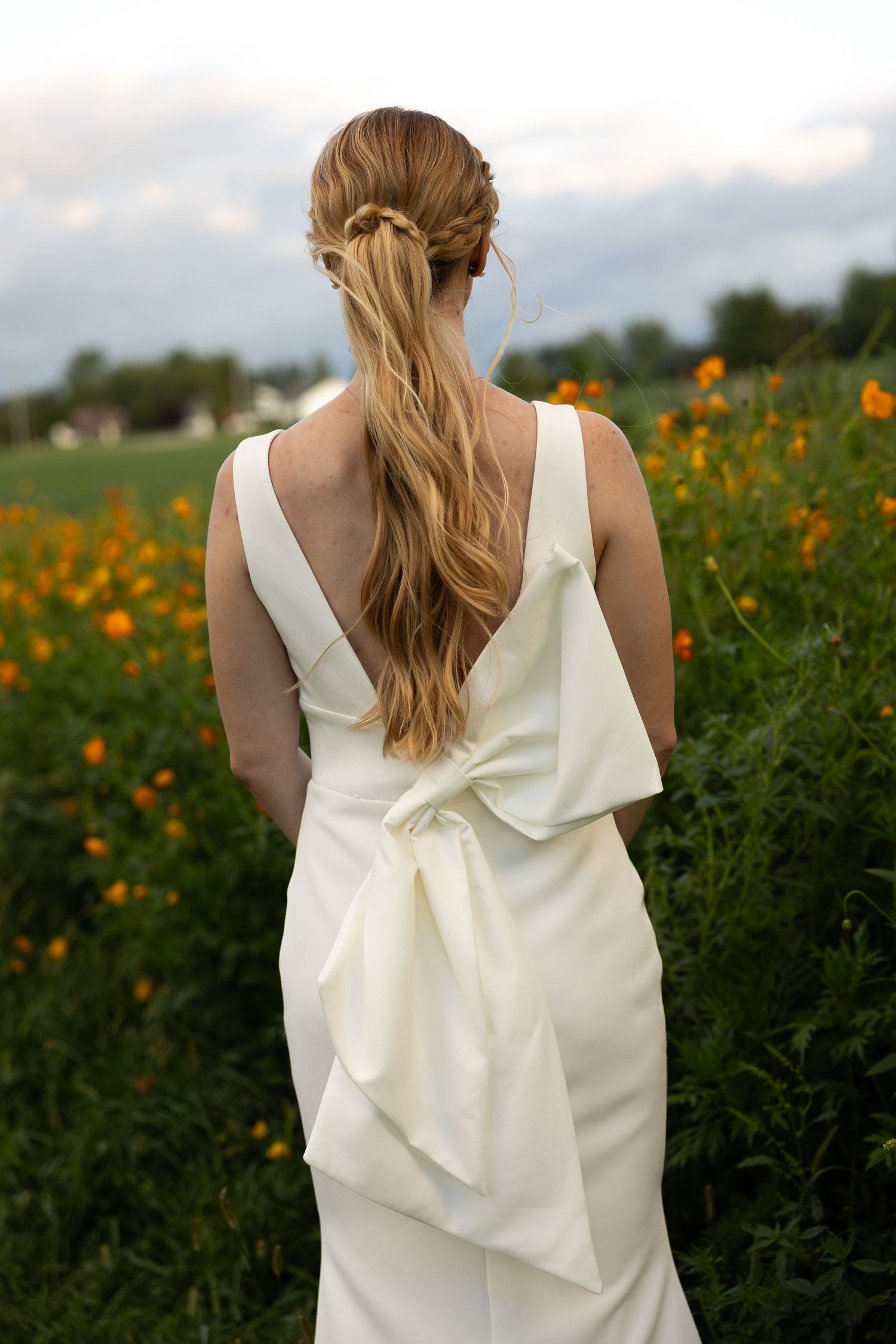 Bride in white dress with dramatic bow detail photographed in wildflower field.