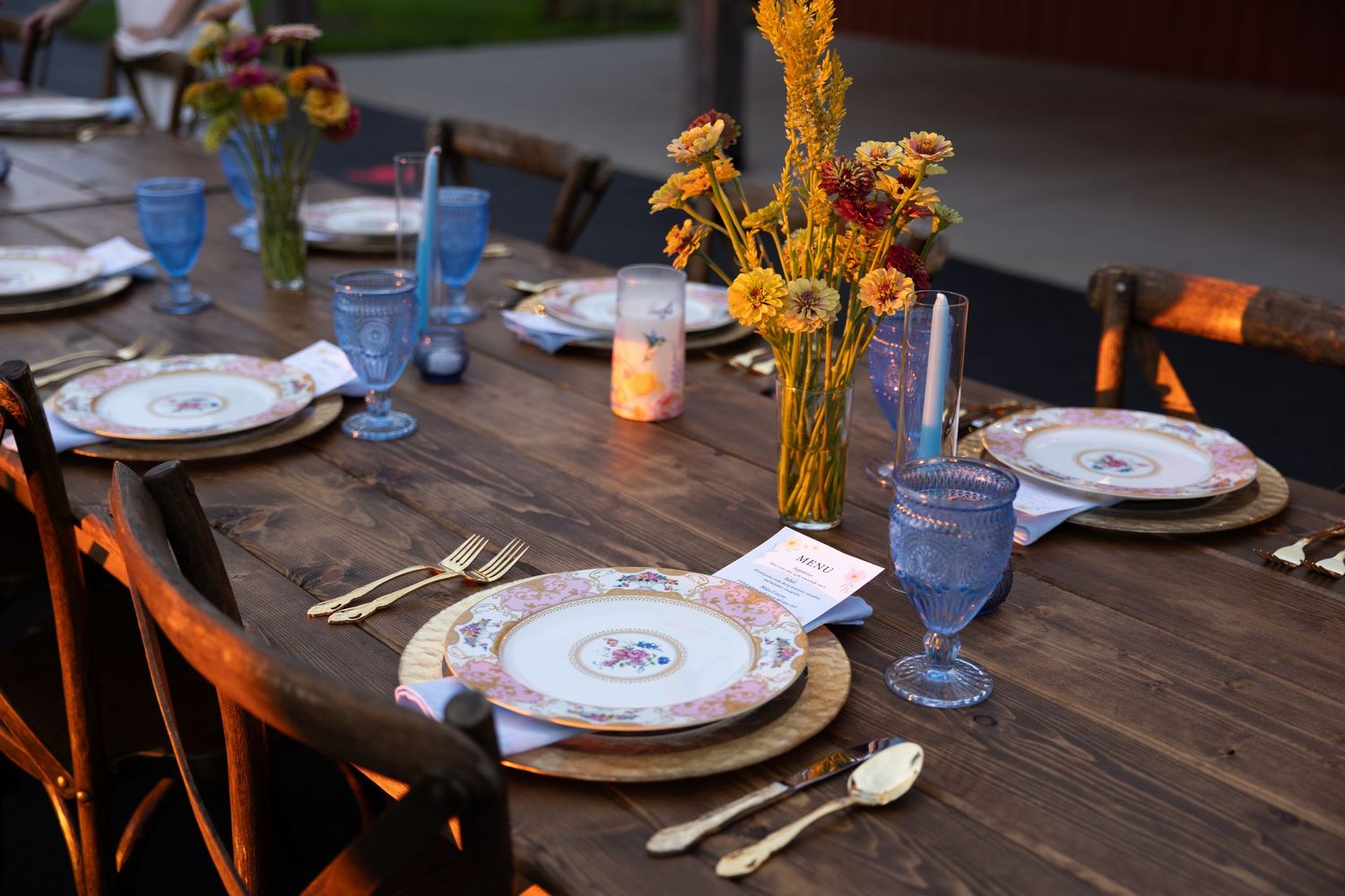 Rustic wooden table set for a wedding reception with vintage plates and candlelight.