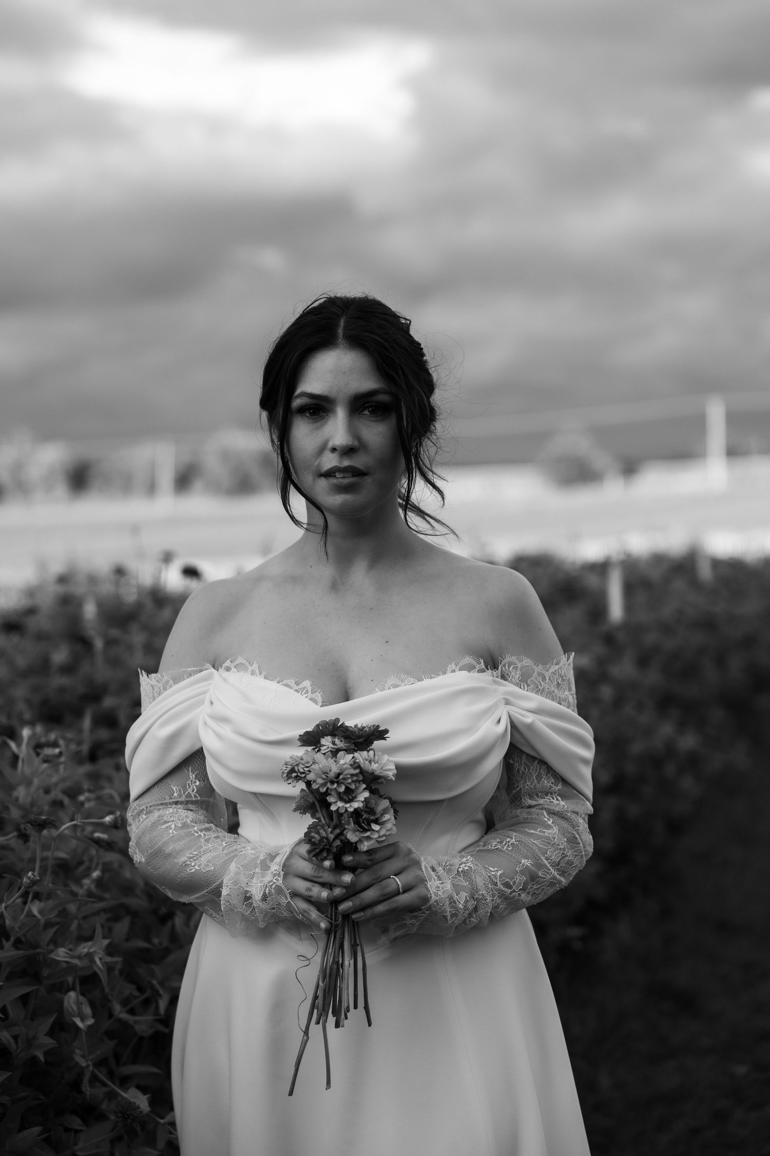 Dramatic black and white bridal portrait with off-shoulder dress and bouquet.