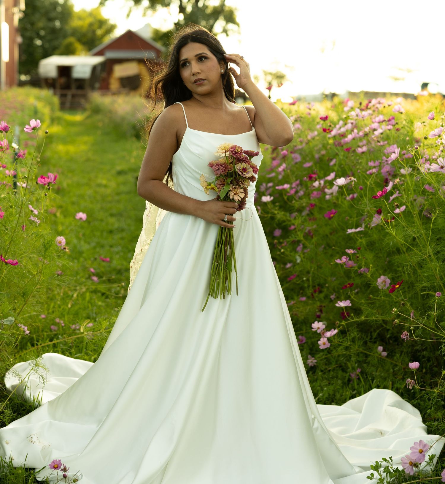 A flowing white wedding dress photographed in a garden with pink cosmos flowers.