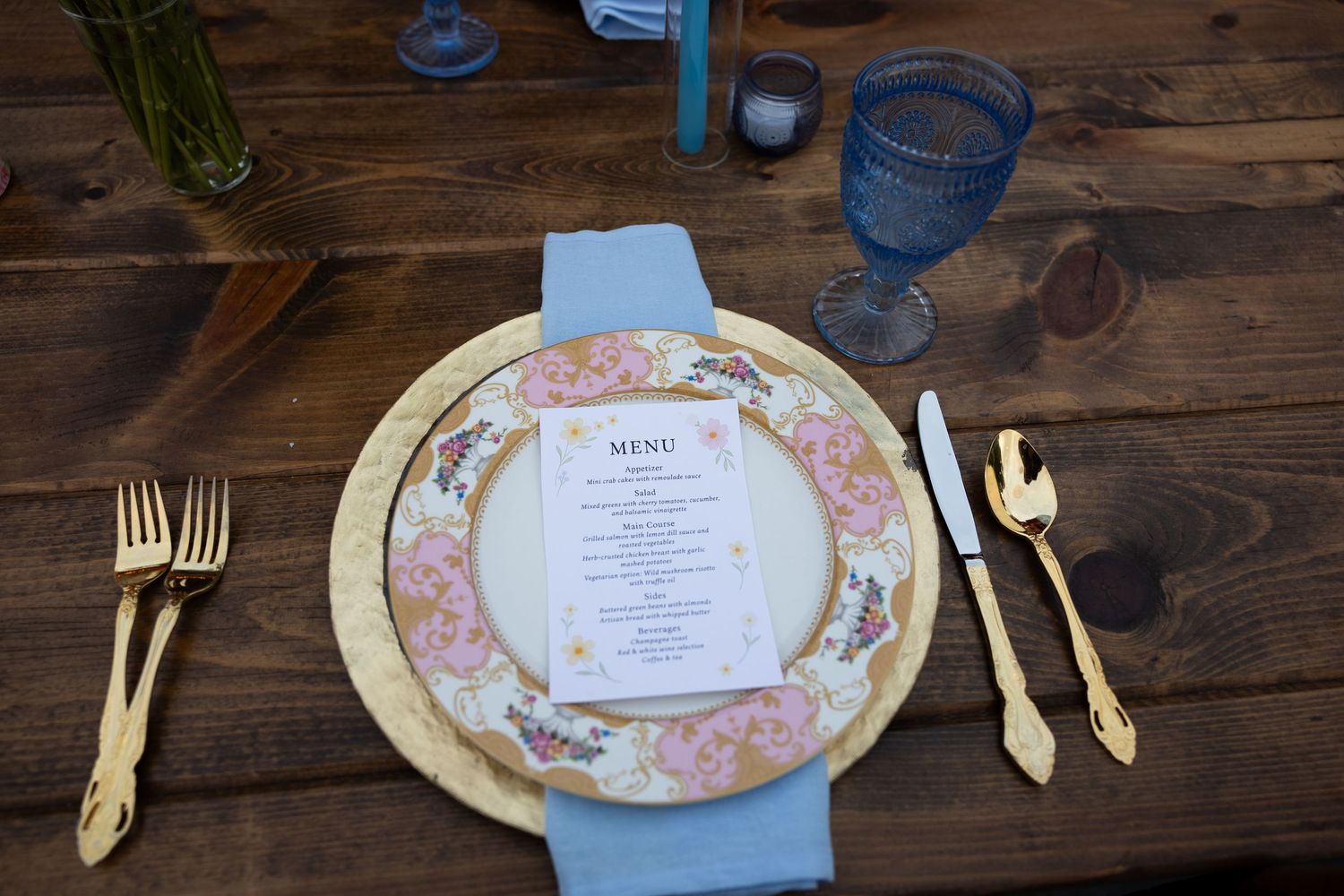 Place settings on a wooden table with floral patterned plates and gold utensils.