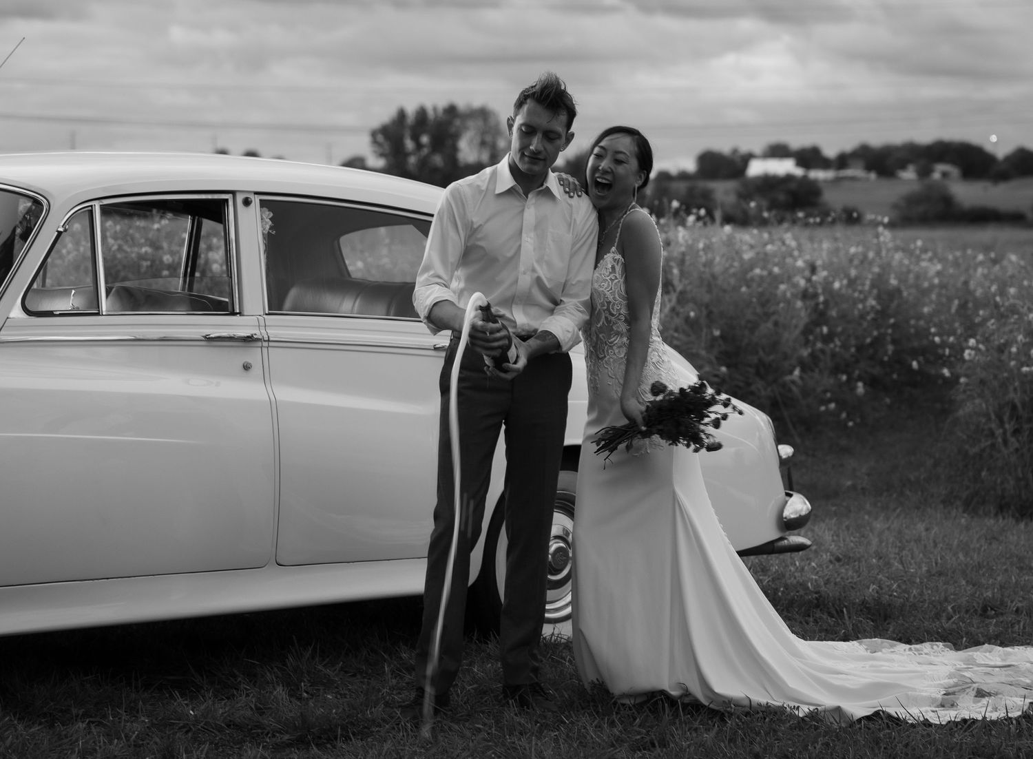 Black and white wedding photography featuring a vintage automobile in a rural setting.