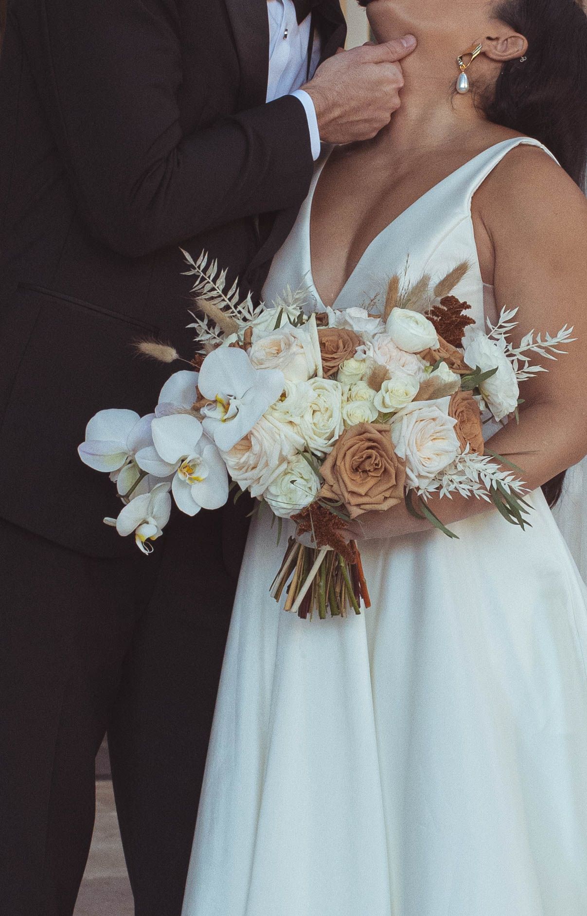 Elegant bridal bouquet with white orchids and neutral roses against white dress.