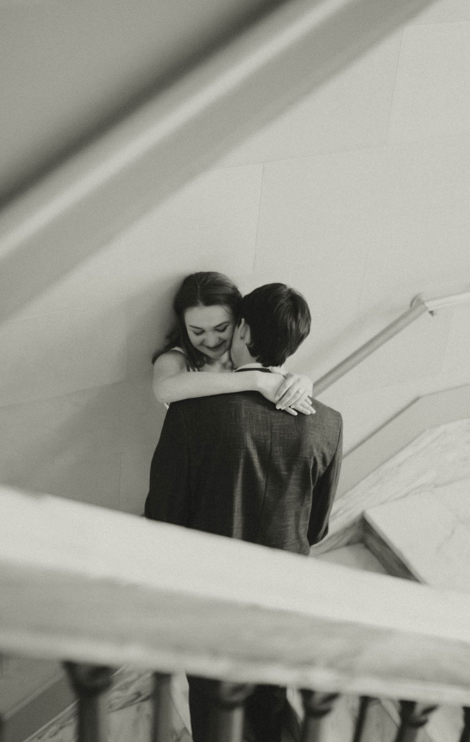 Black and white photo of a couple embracing tenderly on a staircase, the woman smiling warmly.