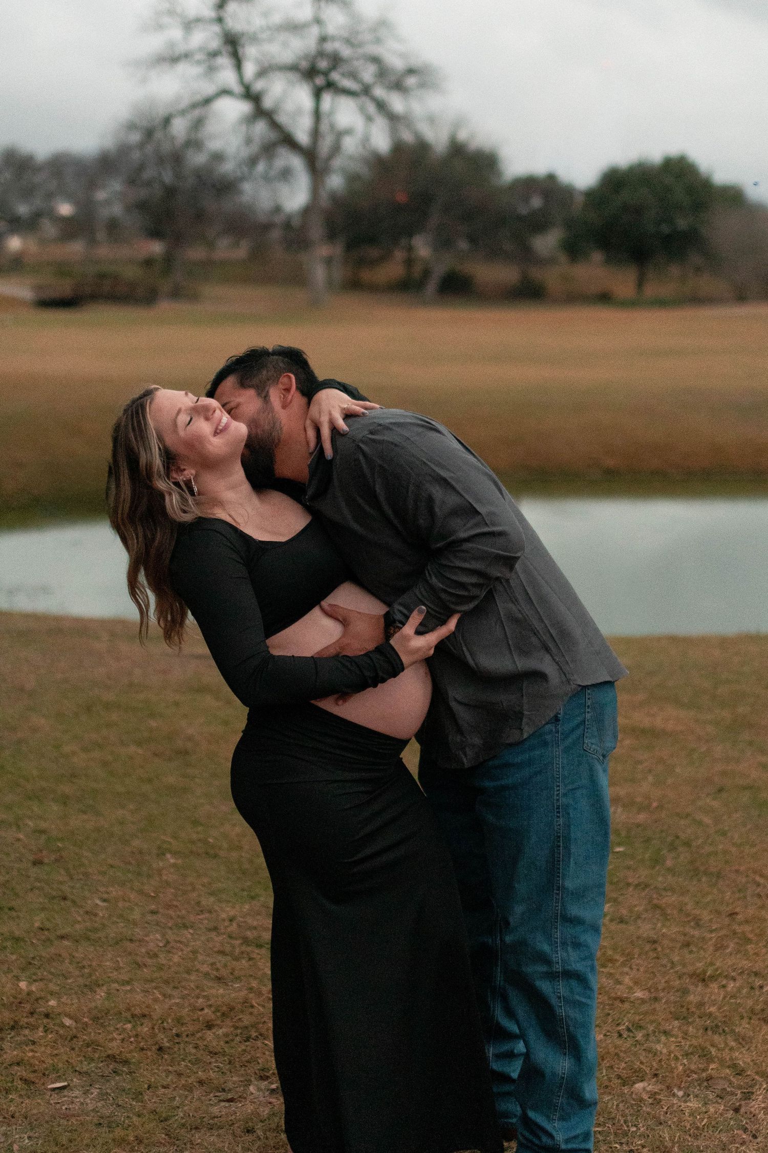 A romantic maternity photo session shows tender moments between an expecting couple by a lake.
