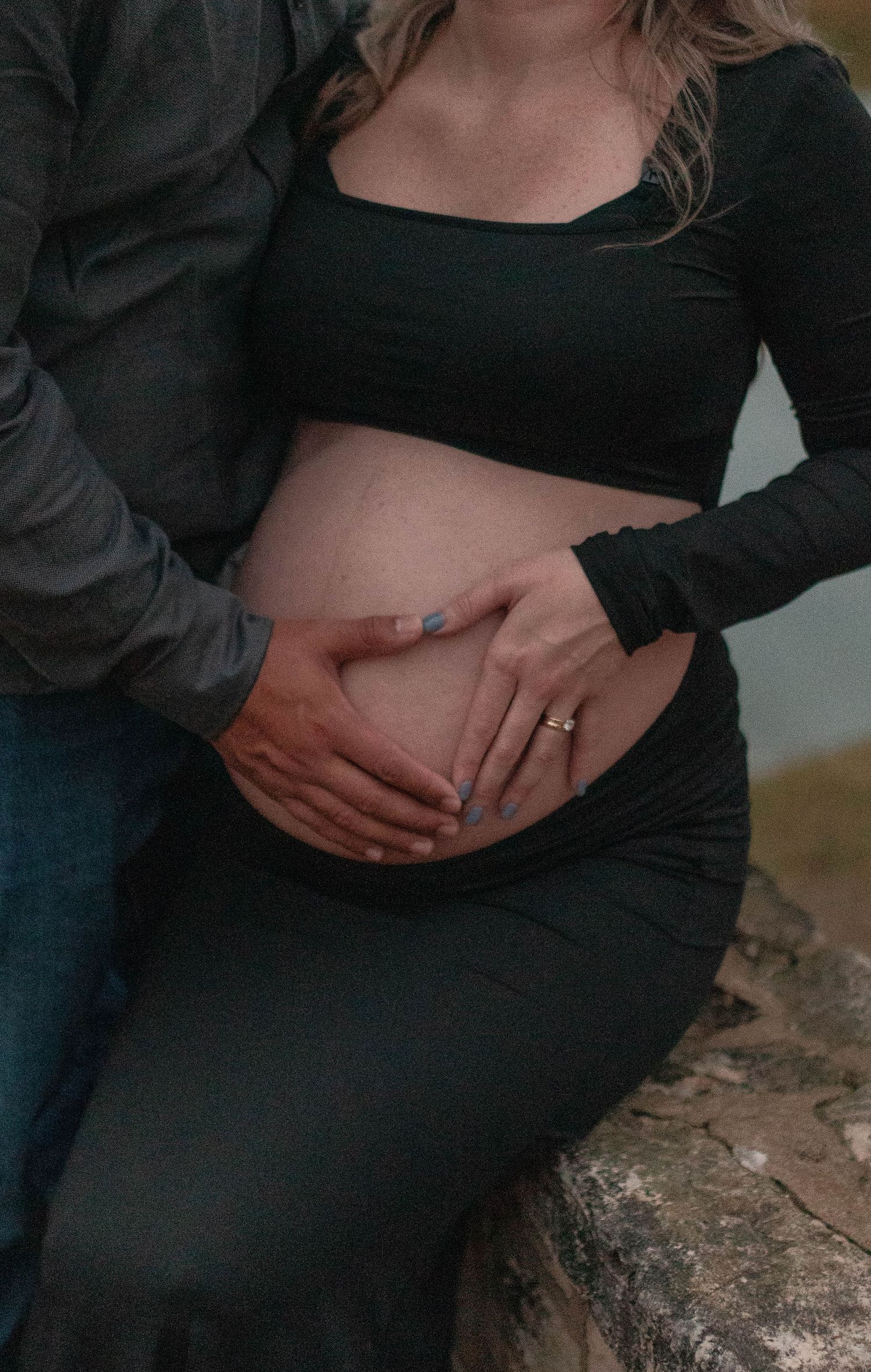 Close-up of hands tenderly cradling a pregnant belly in black clothing.