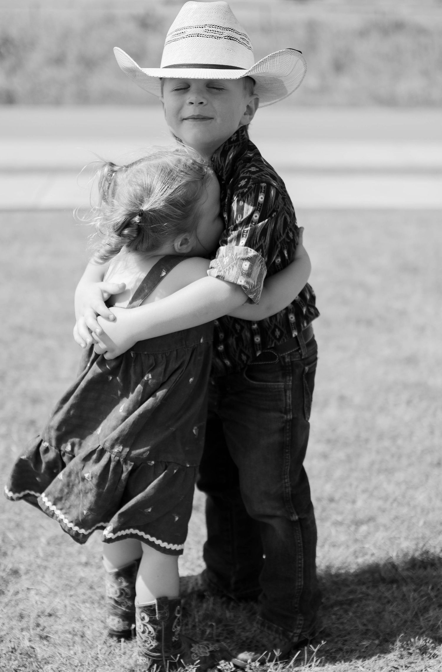 Black and white image of two young children in western wear embracing.