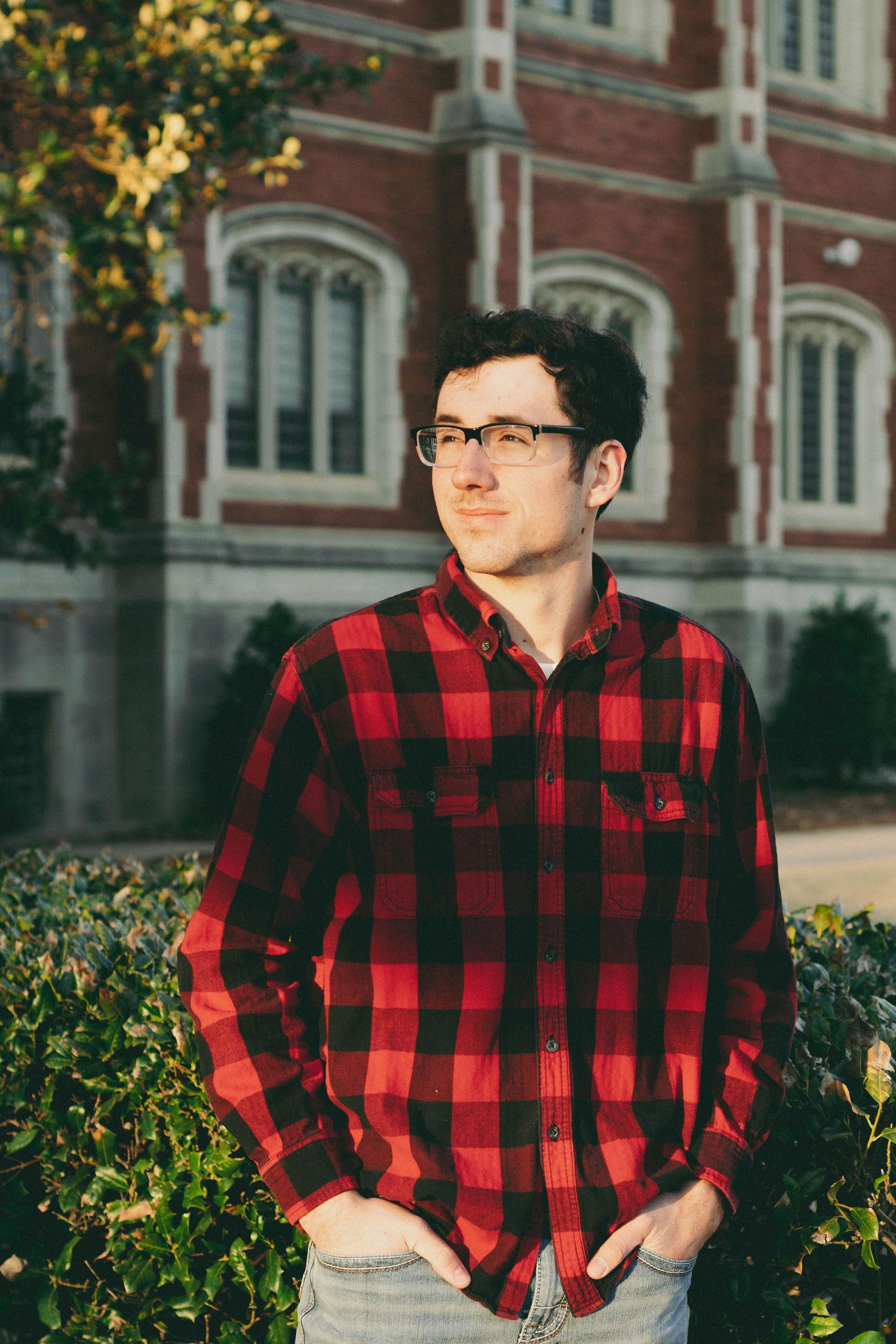 Person in red and black buffalo plaid shirt posing outdoors near brick building.