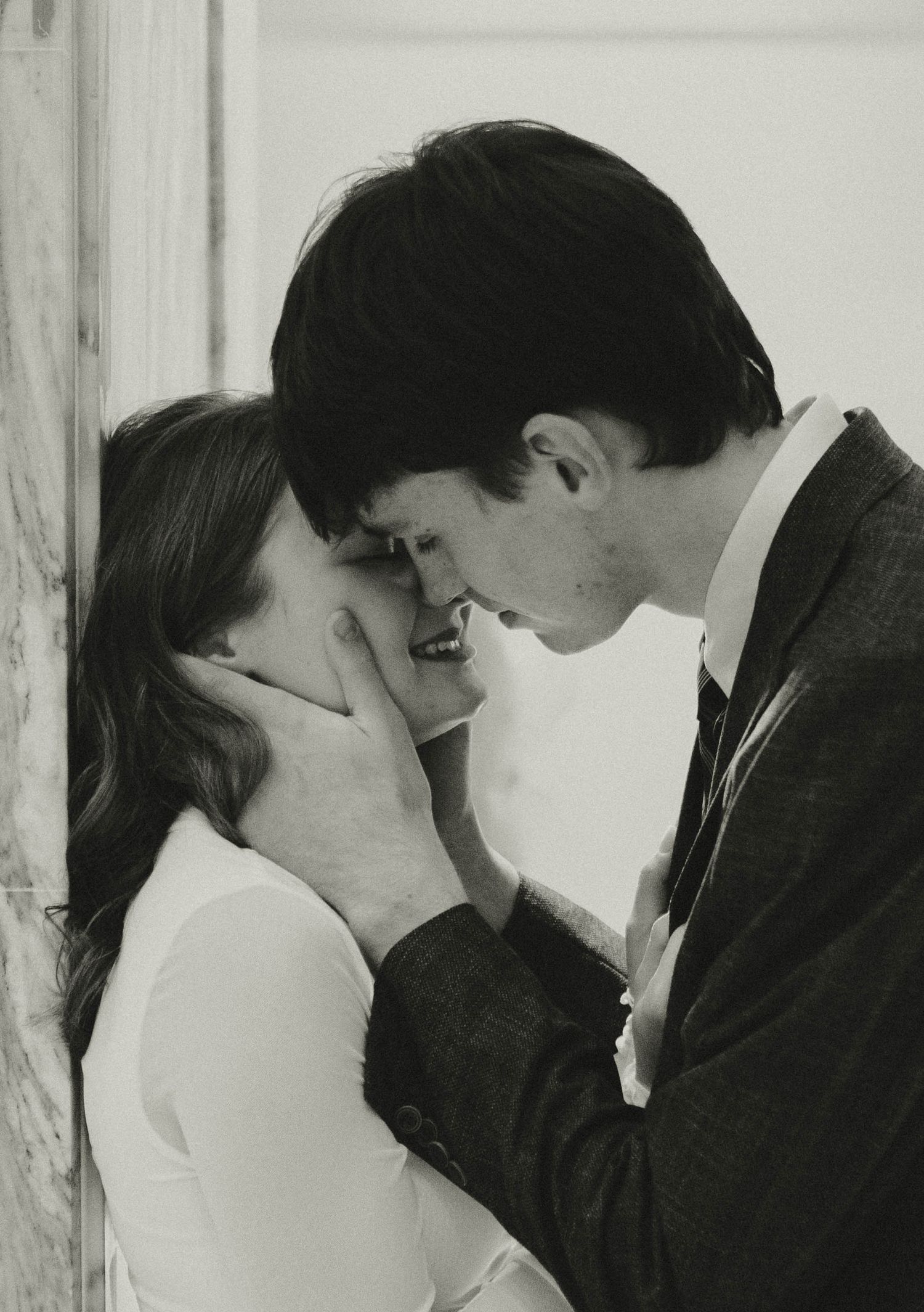Black and white photo of a young couple sharing a romantic moment, man tenderly holding womans face as they lean in to kiss.