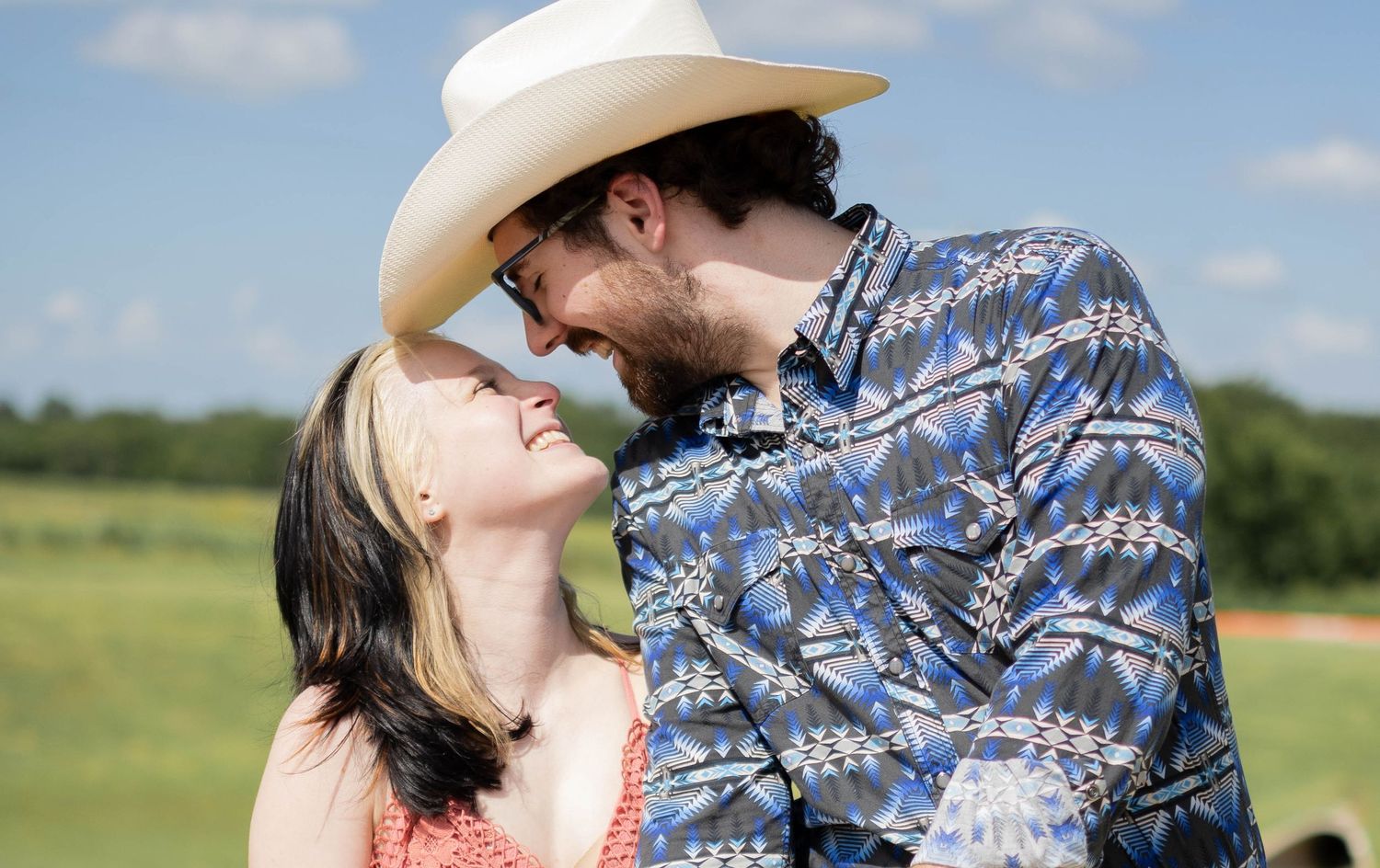 A romantic couple shares tender moments while wearing cowboy hats in a sunny field.