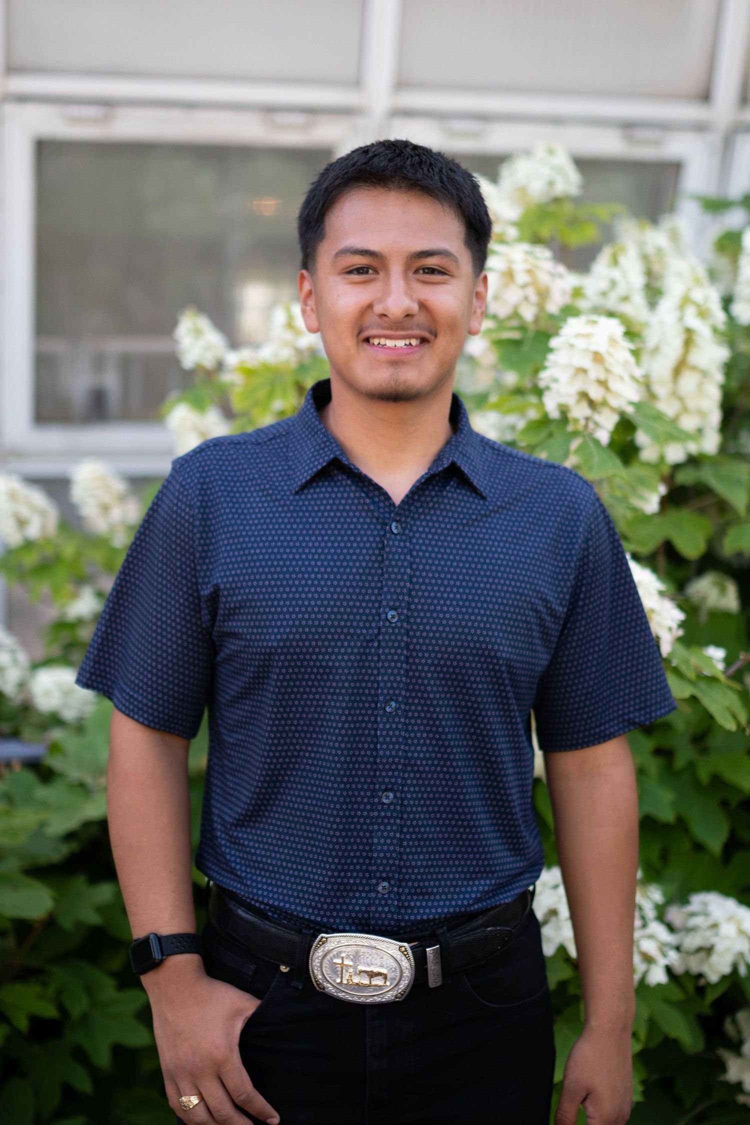 Person in navy polka dot shirt and dark pants standing outdoors near white flowers.