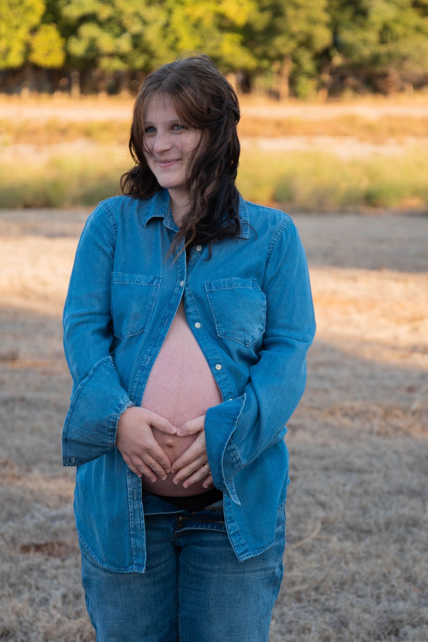 A person in a denim jacket stands in a sunlit field during golden hour.