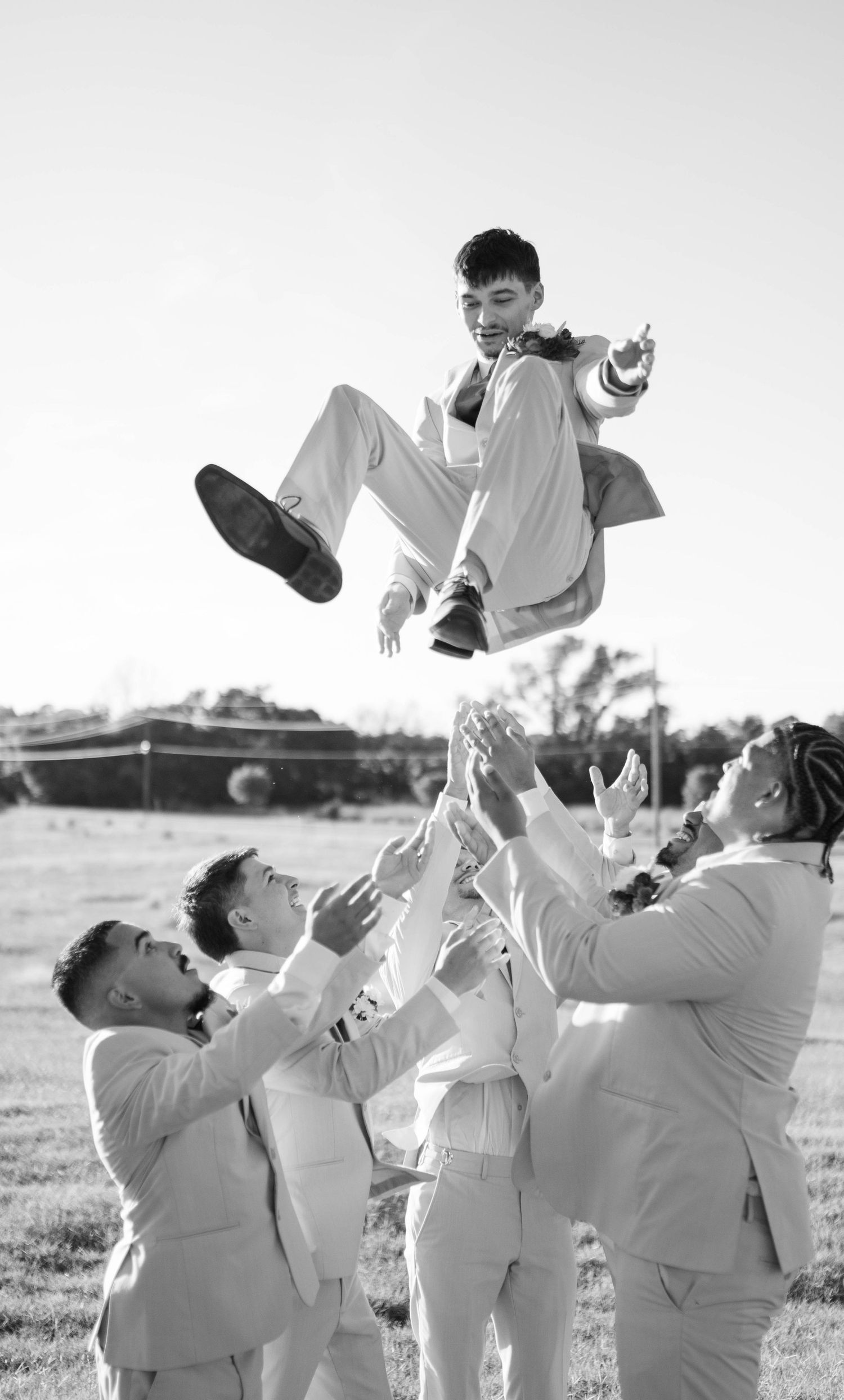 Groomsmen playfully toss groom in the air during outdoor wedding photo session.