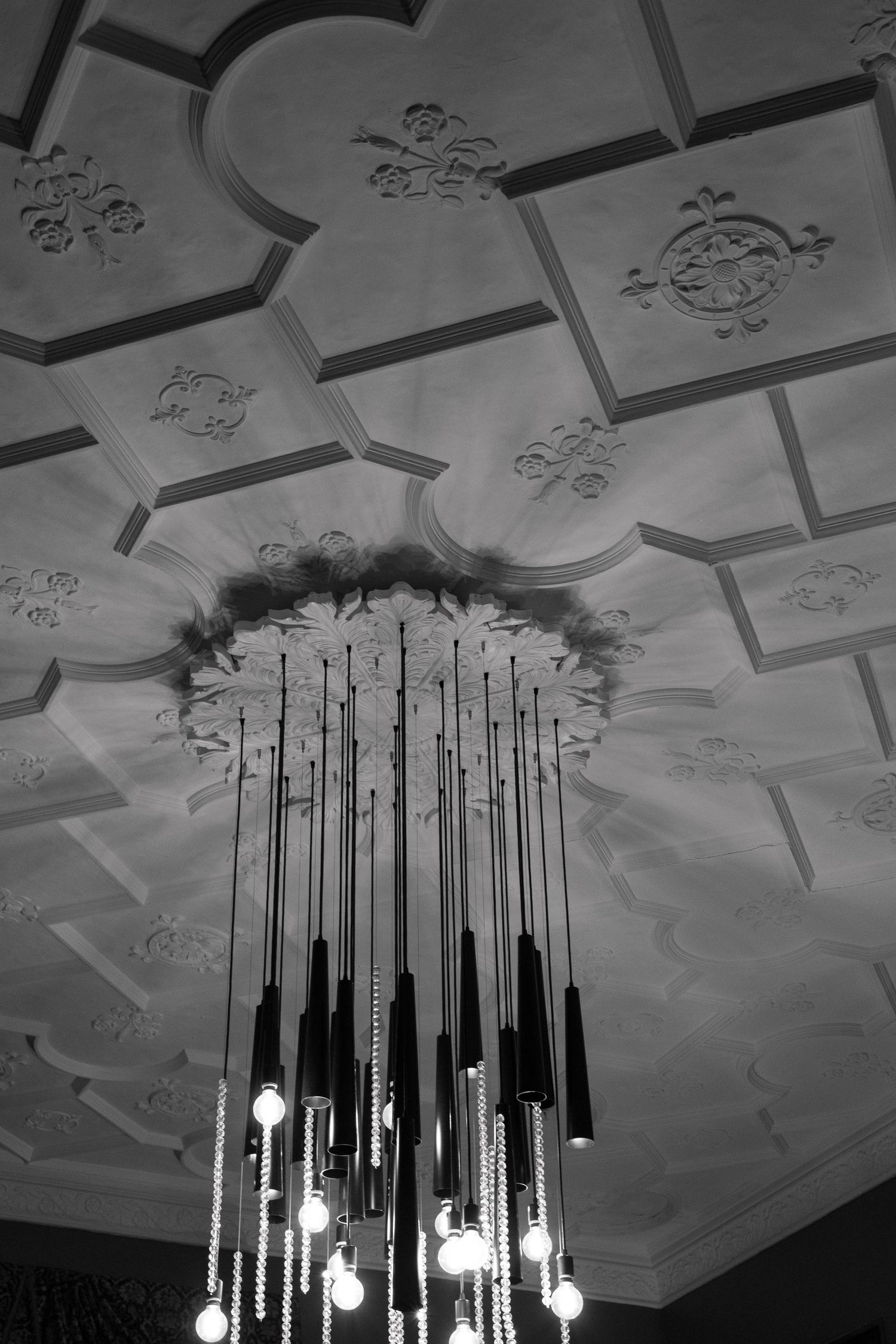 Modern pendant lights hang from an ornate ceiling with decorative moldings in black and white.