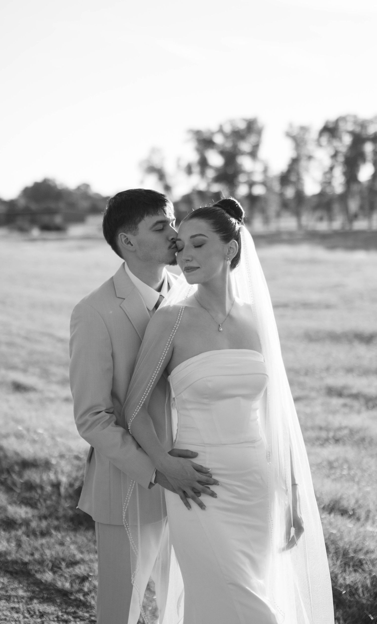 Black and white wedding portraits of couple embracing in outdoor field setting.