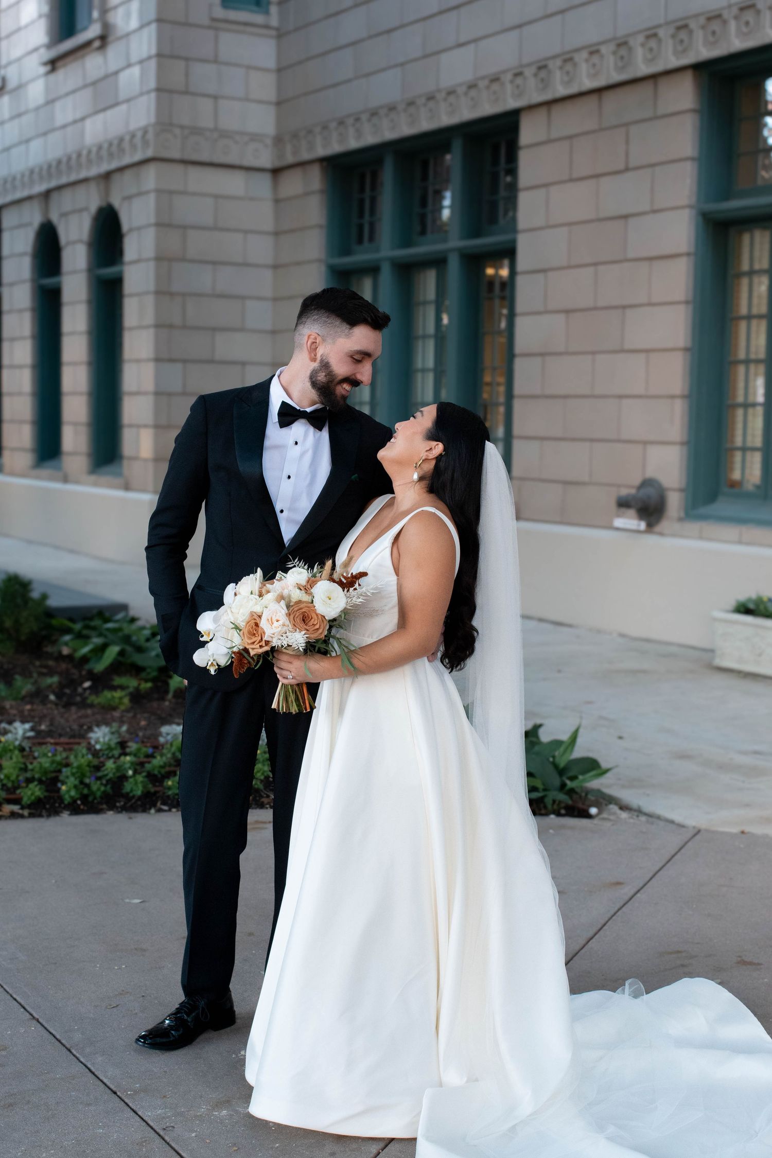 Romantic wedding couple poses outside a grand stone building with architectural details.