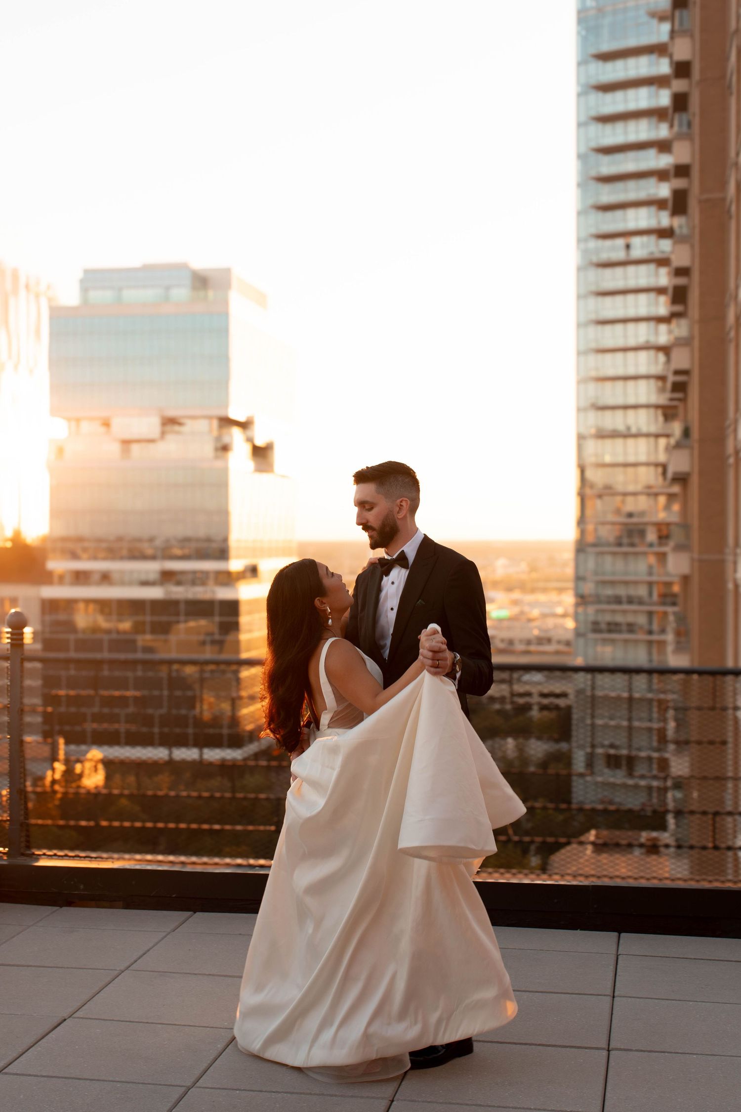 Couple dances on rooftop terrace at sunset with city skyline in background.