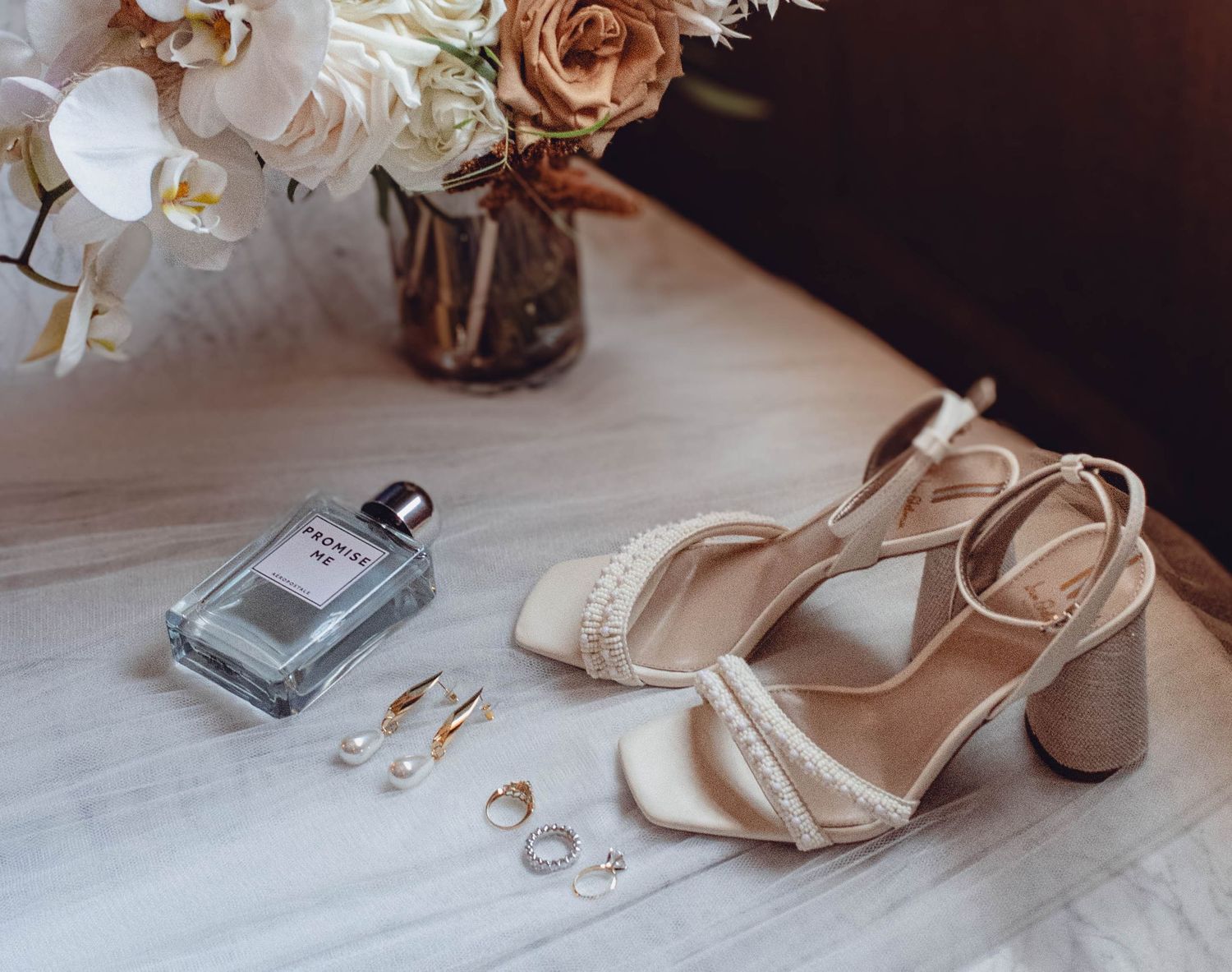 Wedding accessories including flowers, shoes, and rings arranged on a light surface.