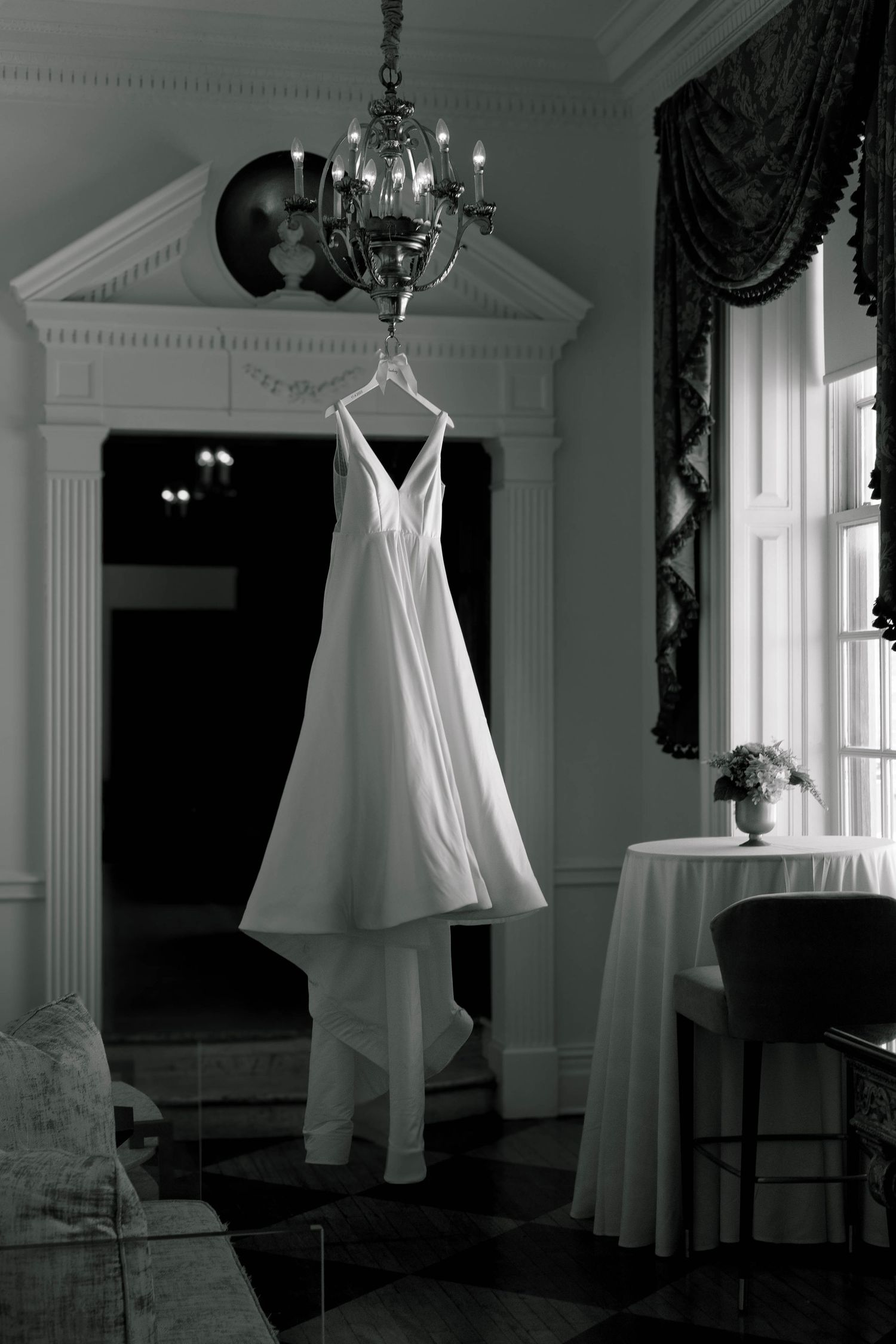A white wedding dress hangs in an elegant room with classical architectural details.