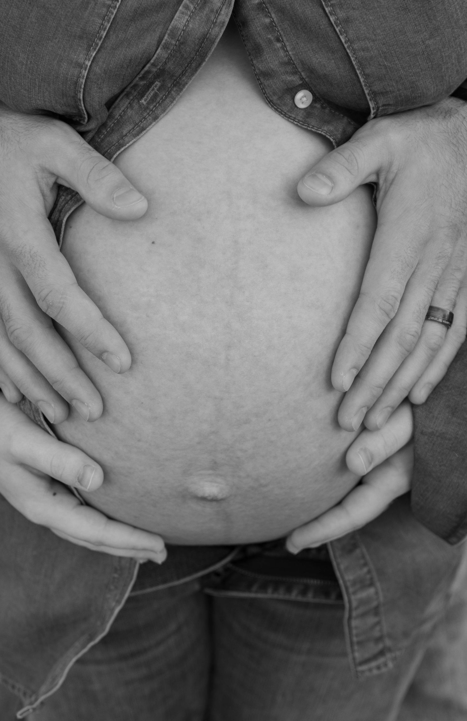 Close-up black and white photo of hands cradling a pregnant belly.
