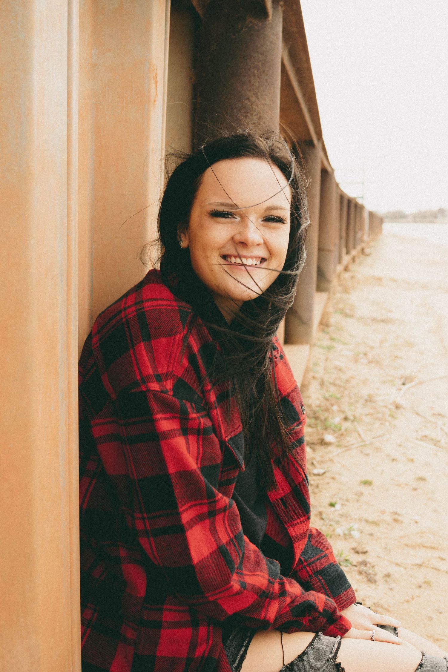 Person in red plaid shirt smiling near pillars in warm sunlight.