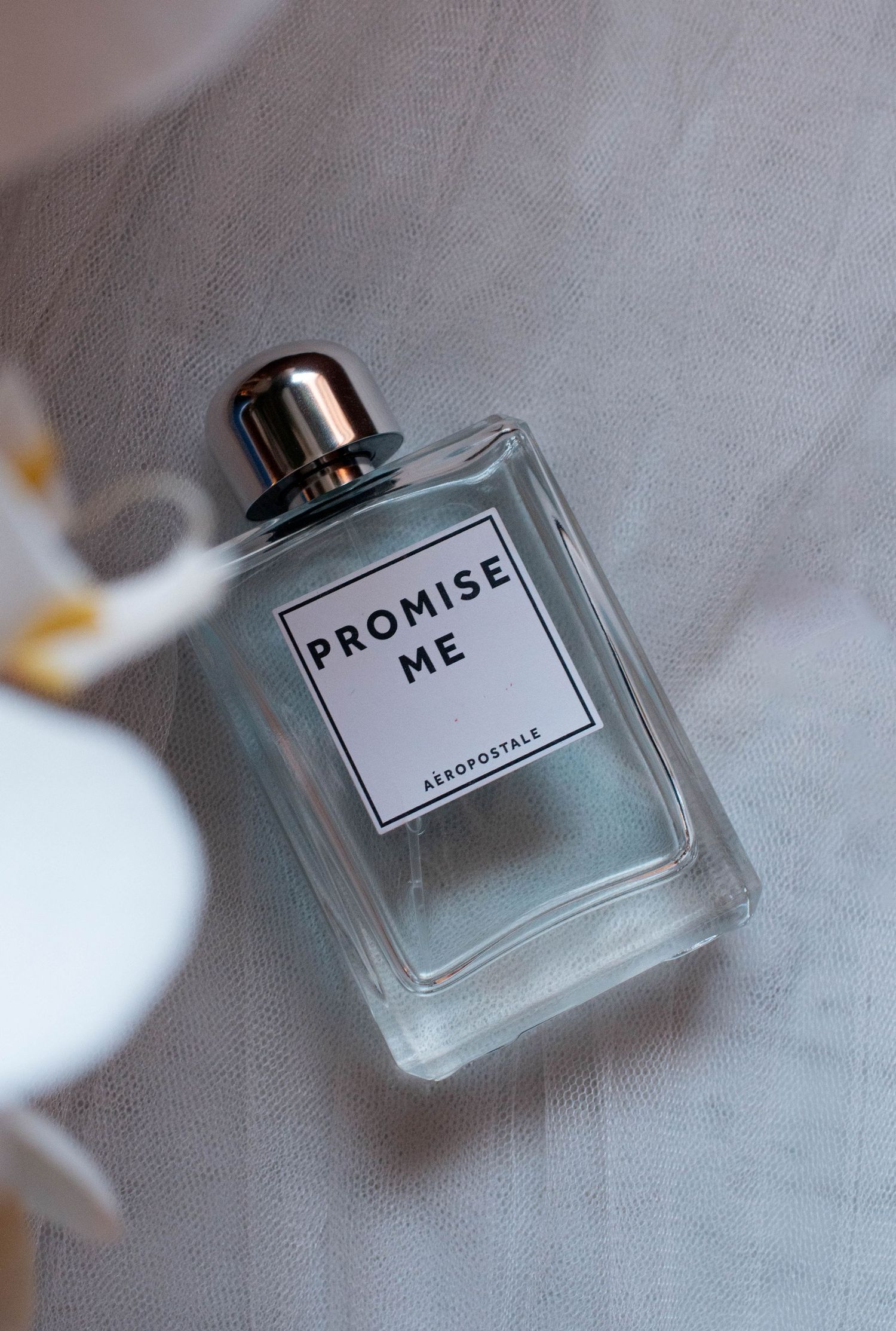 A perfume bottle labeled 'Promise' photographed on a textured fabric surface.