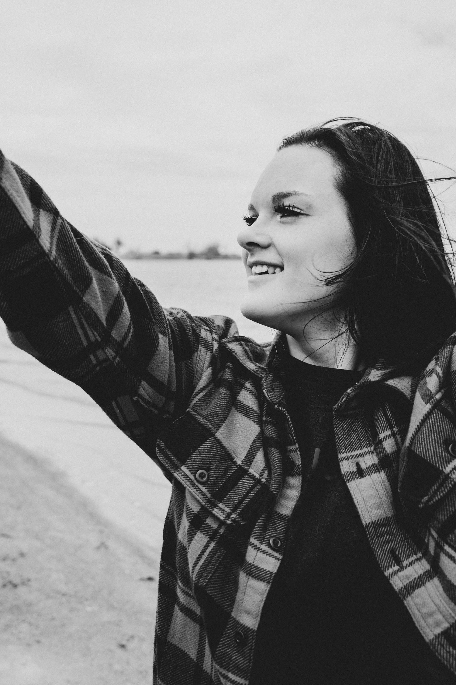 Black and white photo of person in plaid shirt with arms outstretched expressing joy.
