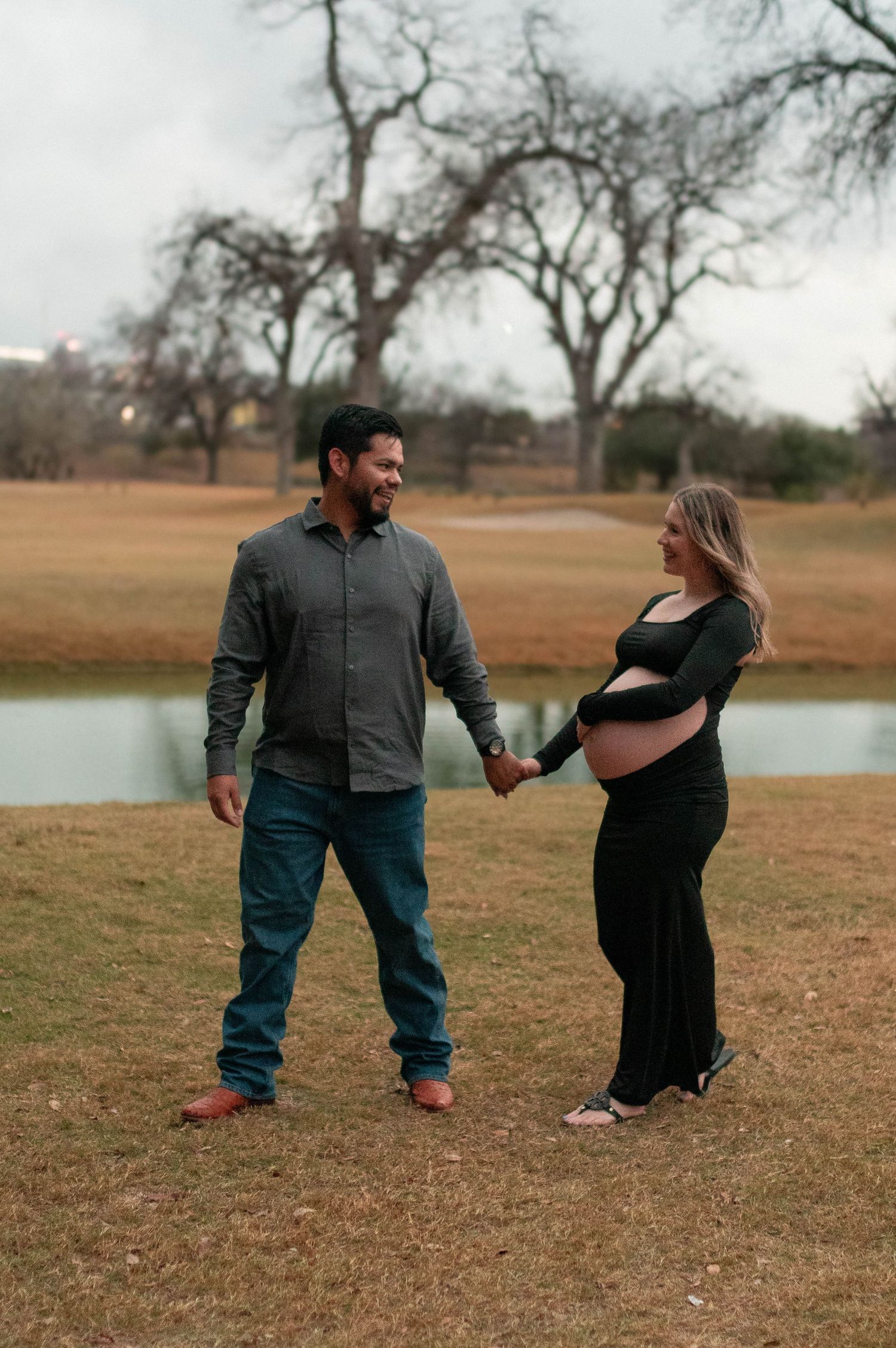 A couple shares a tender moment by a lake during their maternity photoshoot.