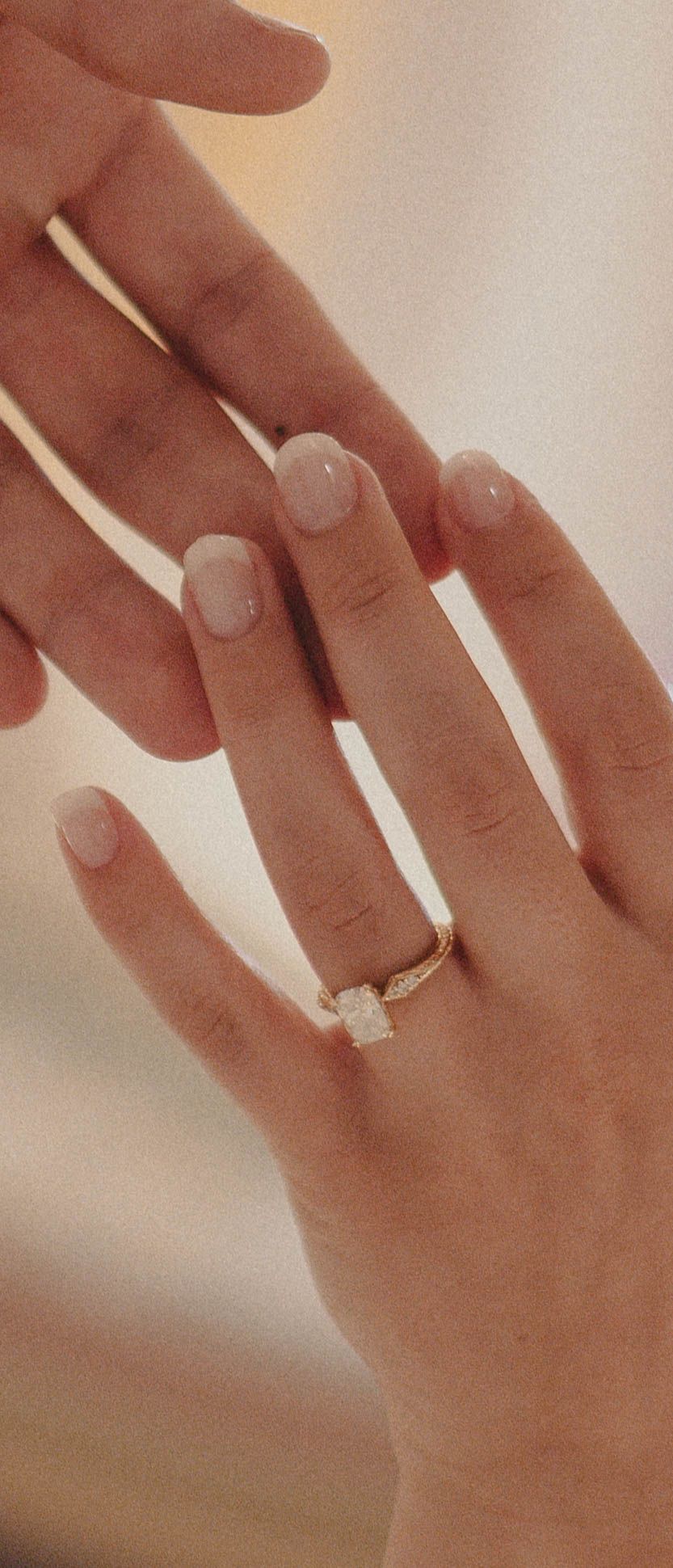 Close-up of elegant hands wearing a gold solitaire diamond engagement ring with delicate side stones on ring finger.
