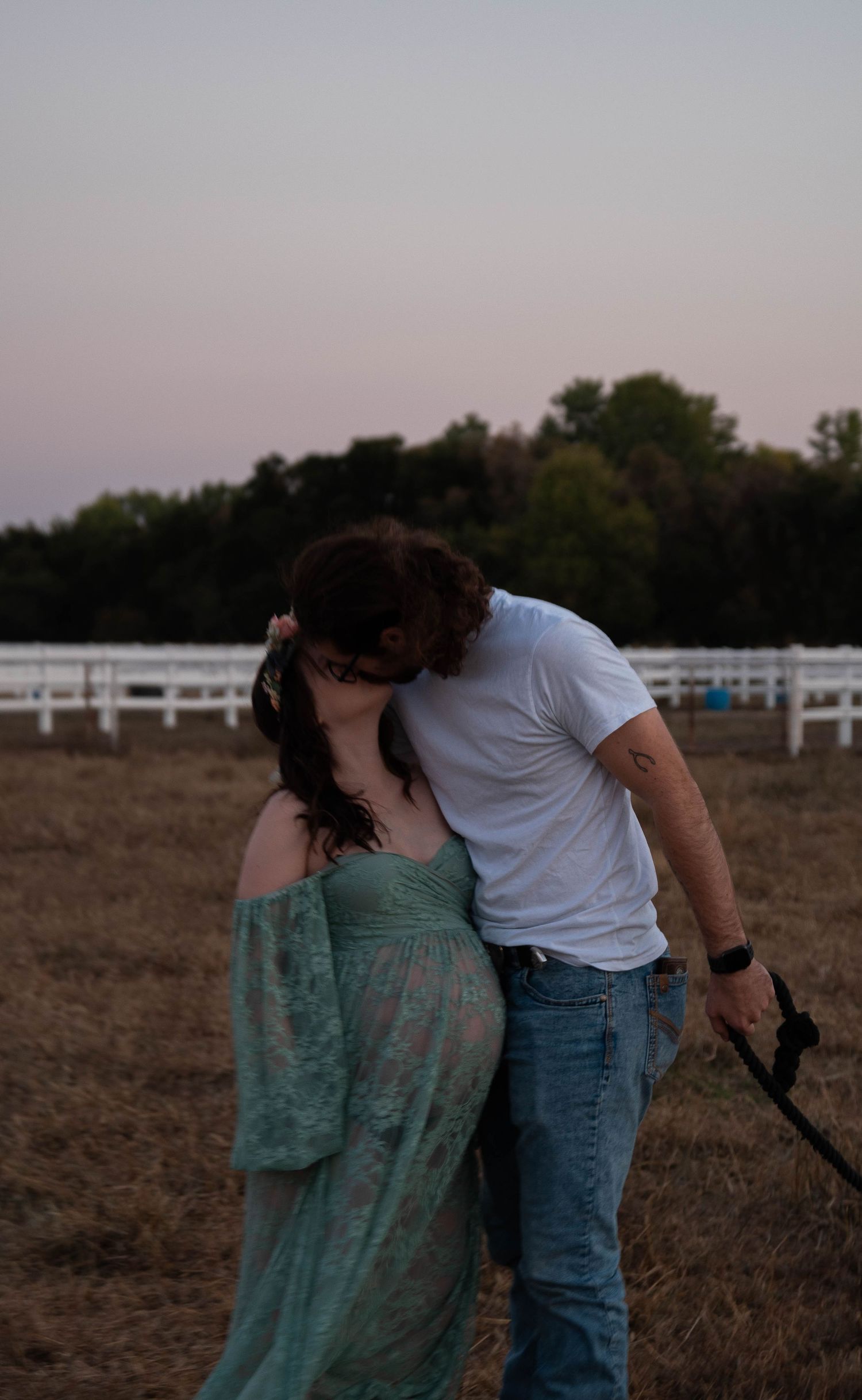 Romantic sunset maternity photo with couple and white horse in field.