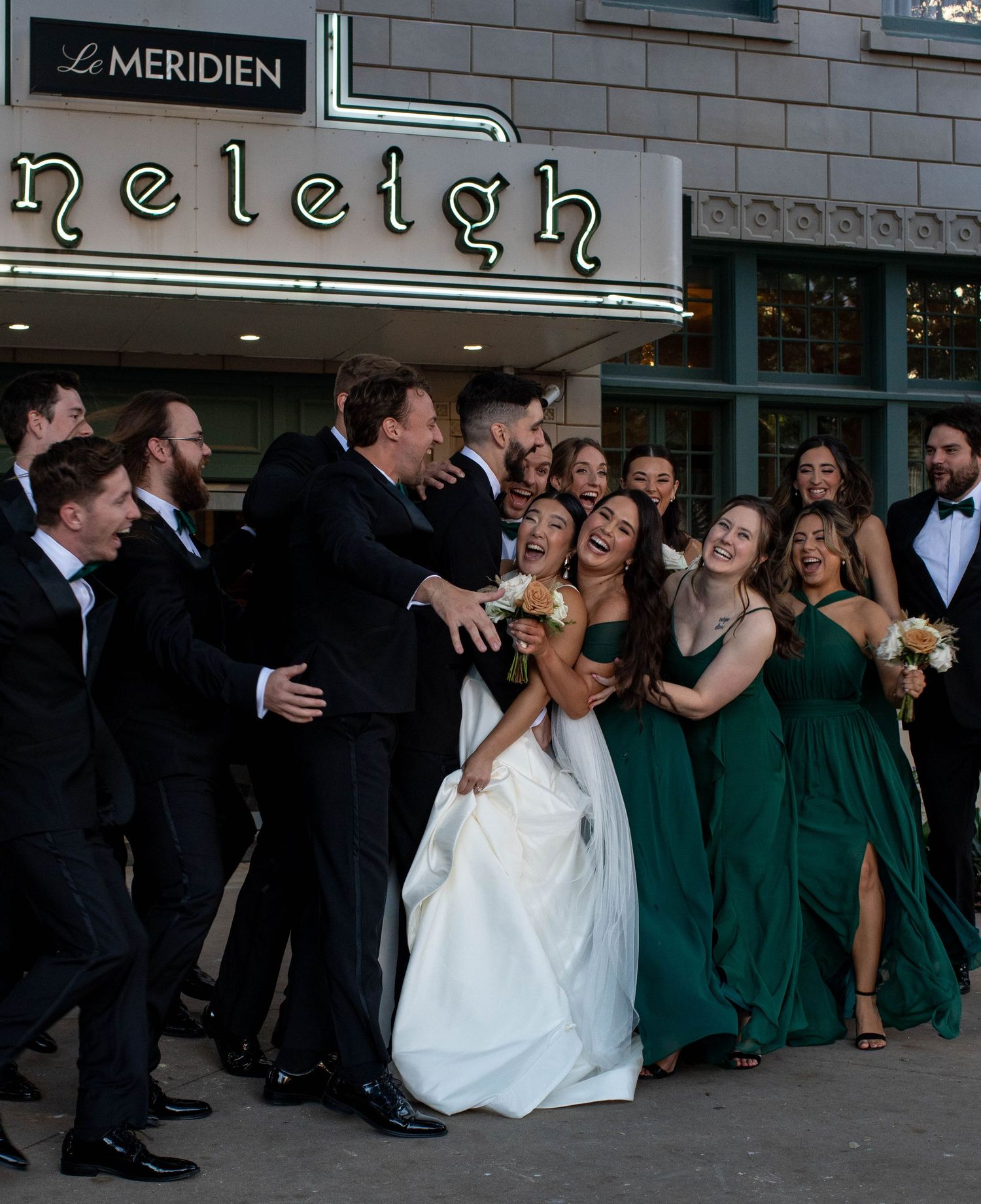 Wedding party celebrates outside Le Meridien hotel with bridesmaids in emerald green dresses.